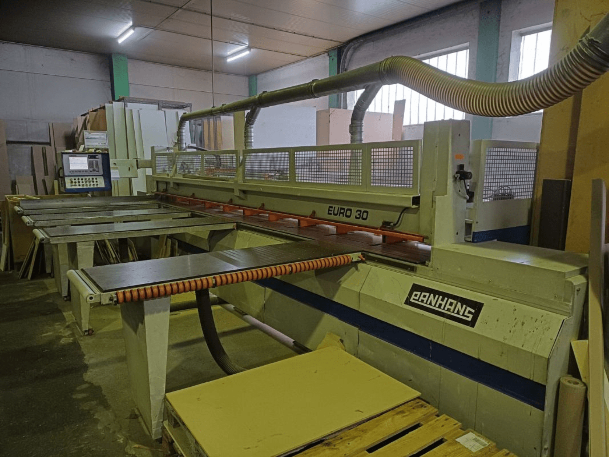 Vista frontal da serra de painel PANHANS EURO 30 com painel de controlo, mesa de corte e mangueira de extração de poeiras numa oficina.