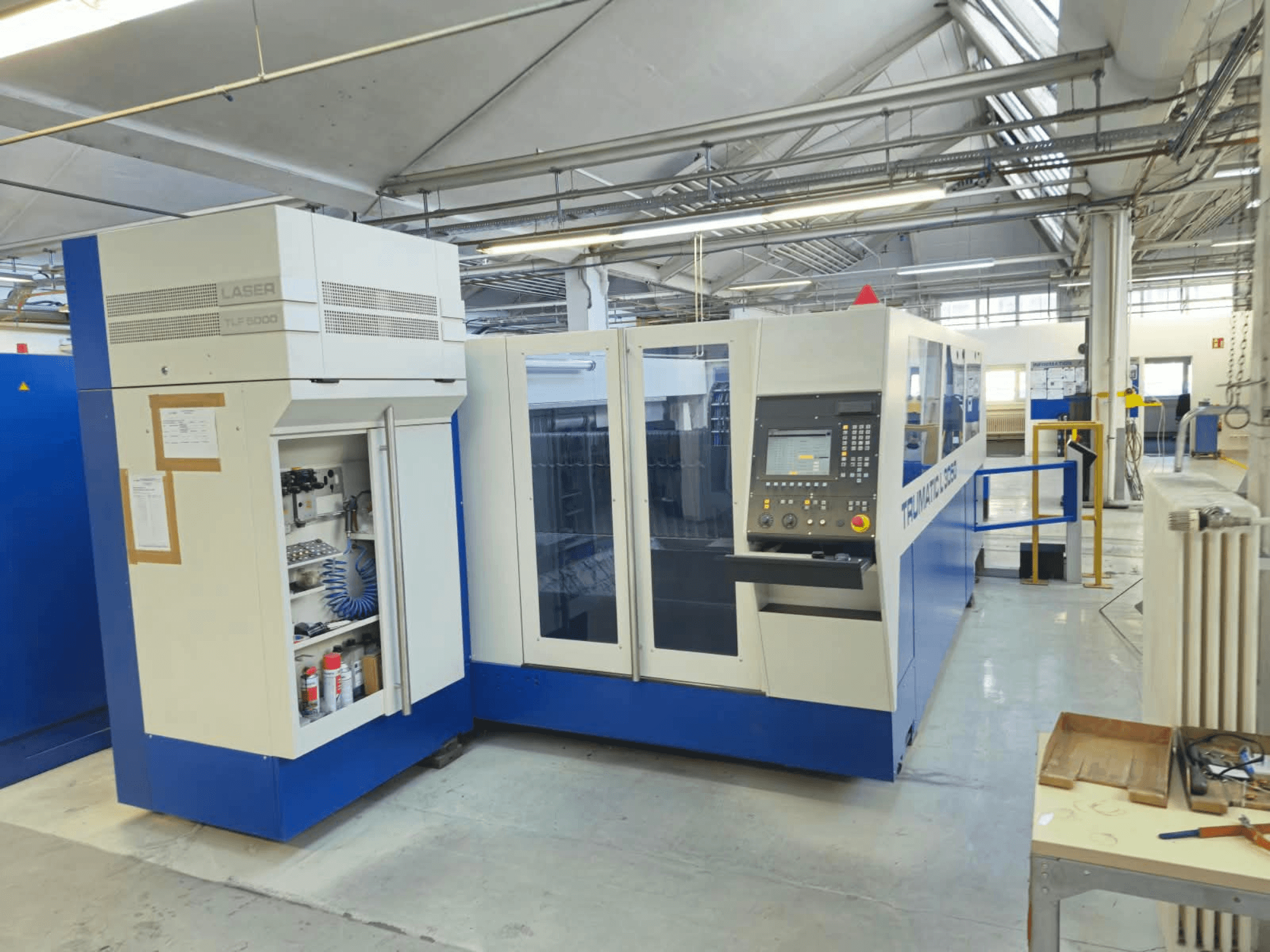 Máquina de corte a laser de CO₂ TRUMPF TruLaser L3050, vista frontal, com painel de controlo e porta de acesso para manutenção, num ambiente de fábrica.