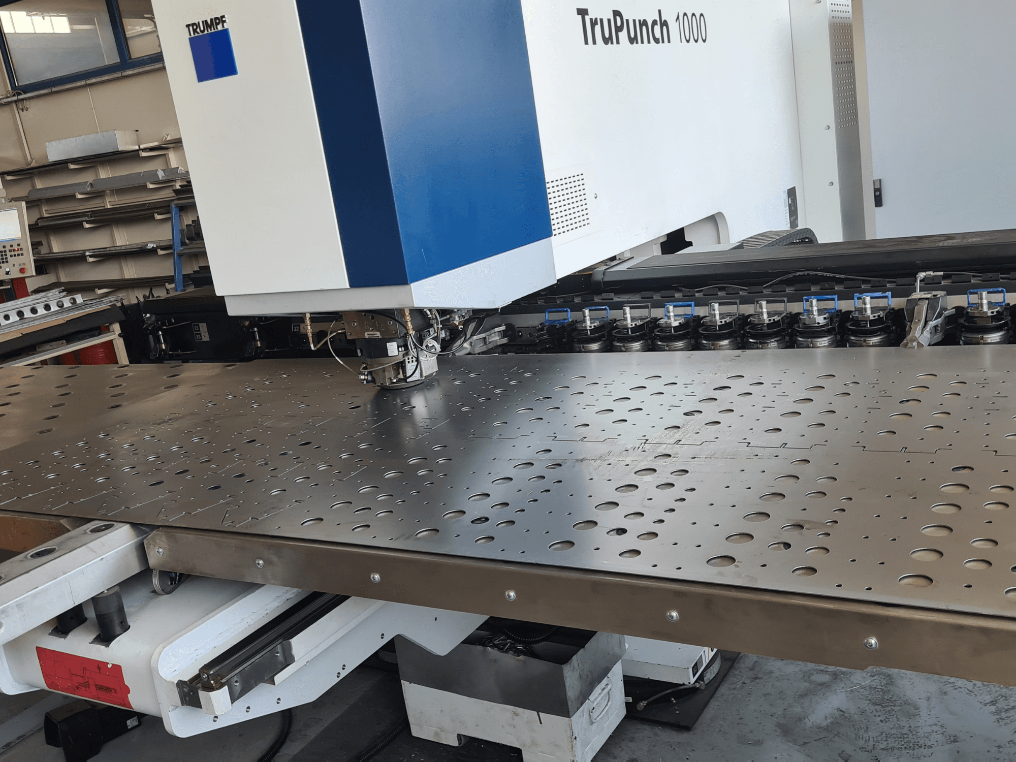 Máquina de perfuração CNC TRUMPF TruPunch 1000, vista frontal, mostrando uma chapa metálica perfurada e a configuração da ferramenta.