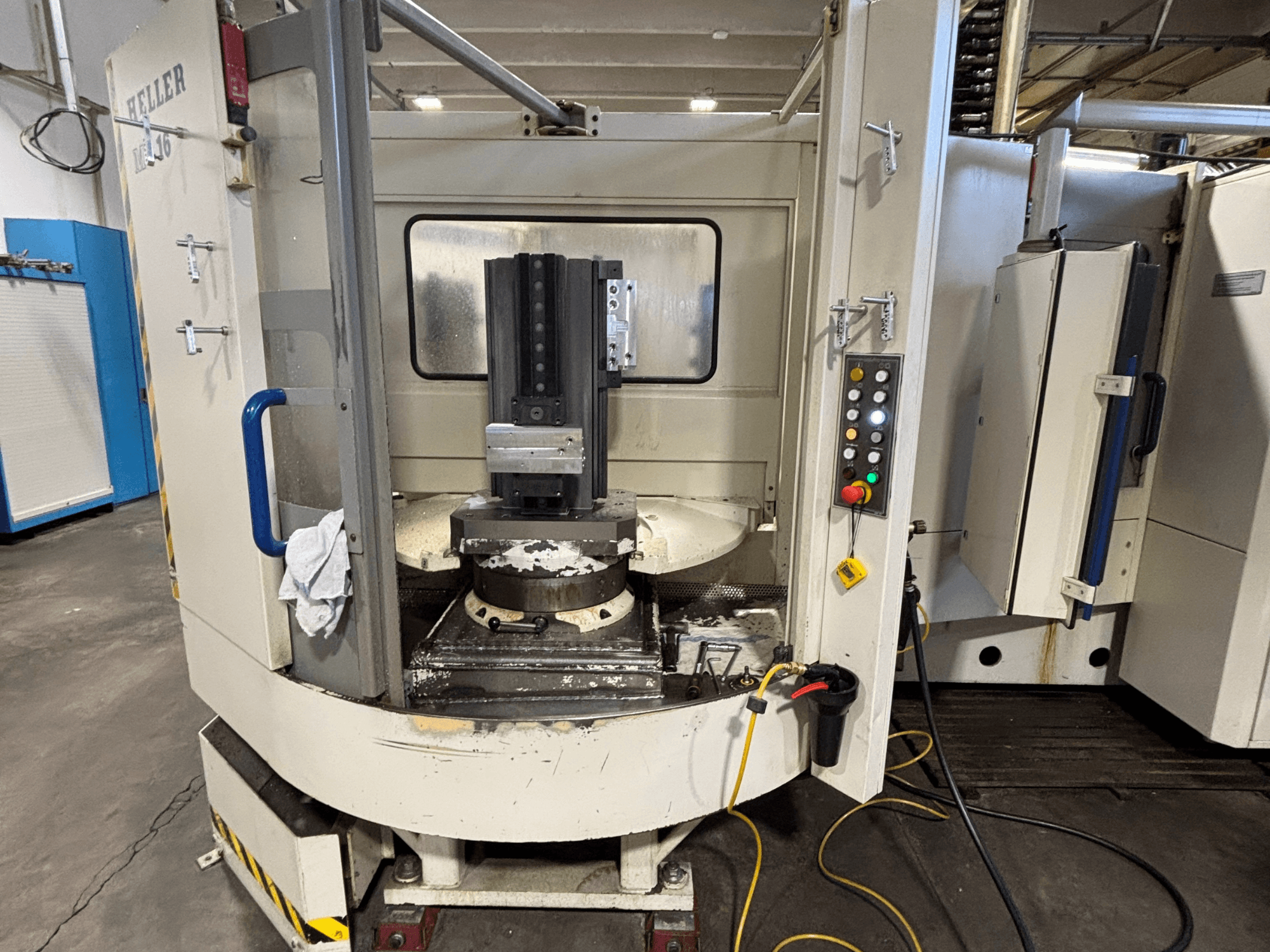 Centro de maquinação Heller, modelo vertical, vista frontal mostrando o fuso, o painel de controlo e a mesa de trabalho com o equipamento acoplado.