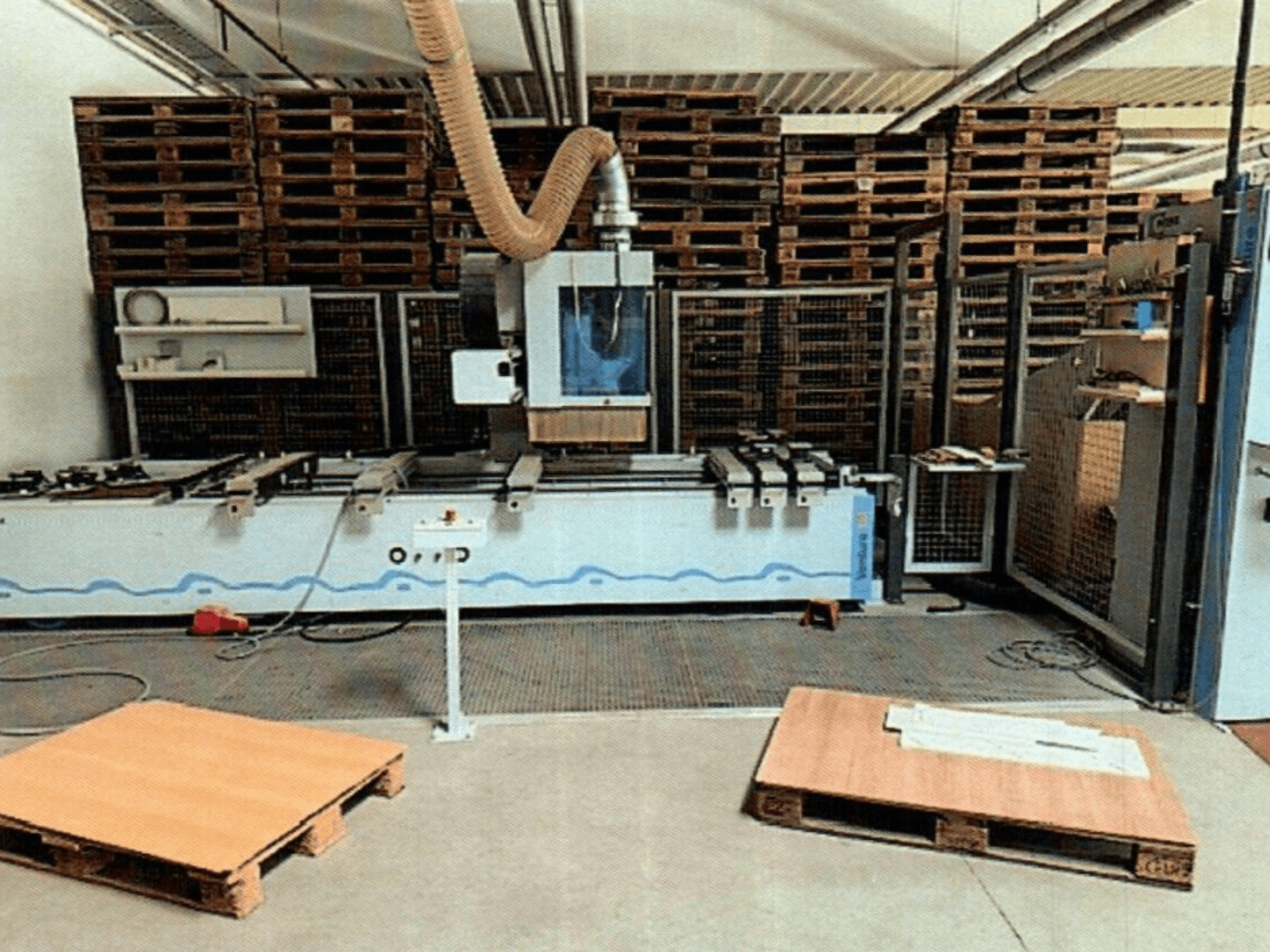 Centro de maquinação CNC para madeira Weeke Venture 1M numa oficina, vista frontal com paletes de madeira visíveis e configuração industrial.