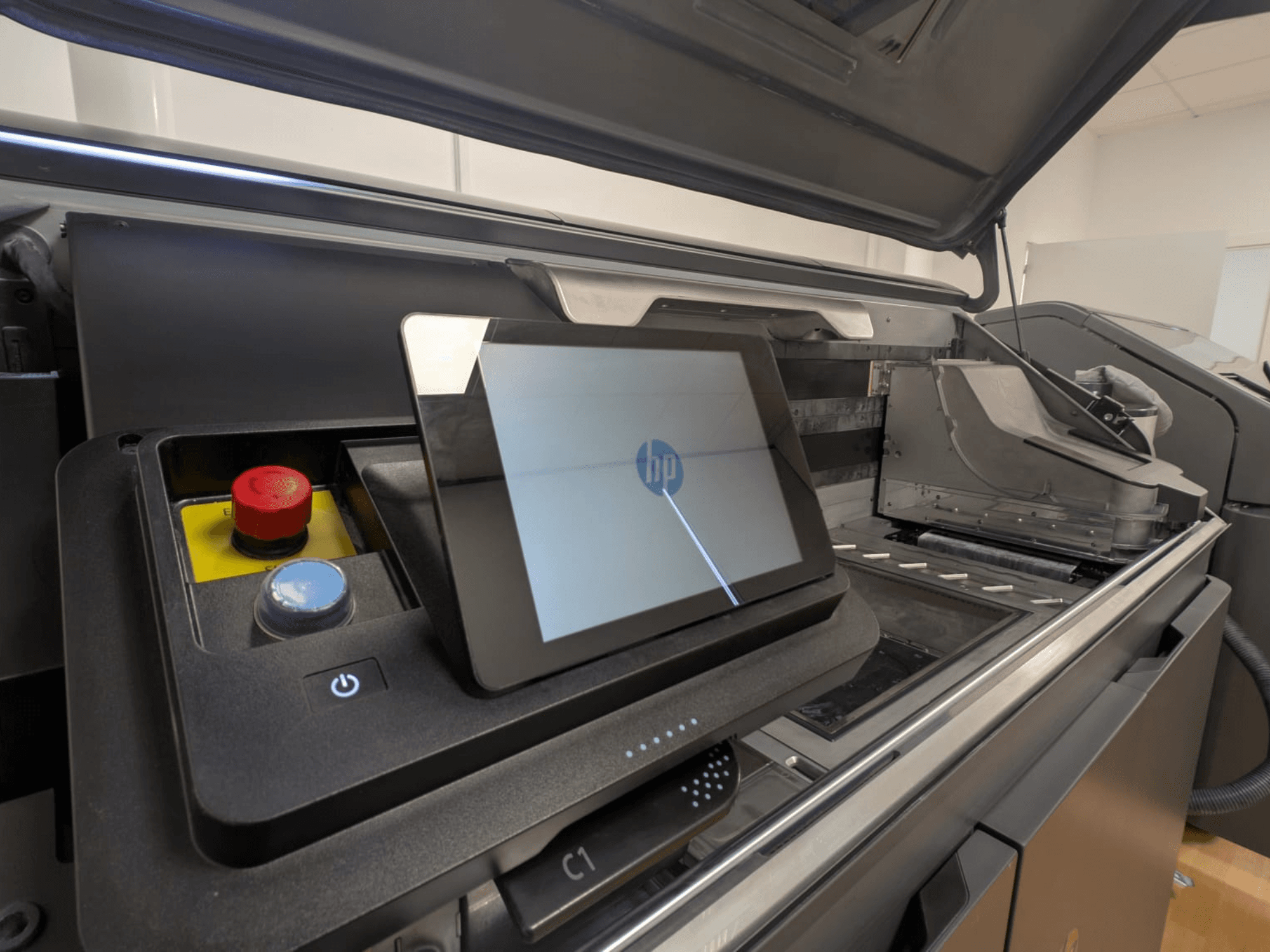 Painel de controlo da impressora HP com um ecrã de tablet, botões vermelhos e azuis e uma vista lateral dos componentes interiores da impressora.