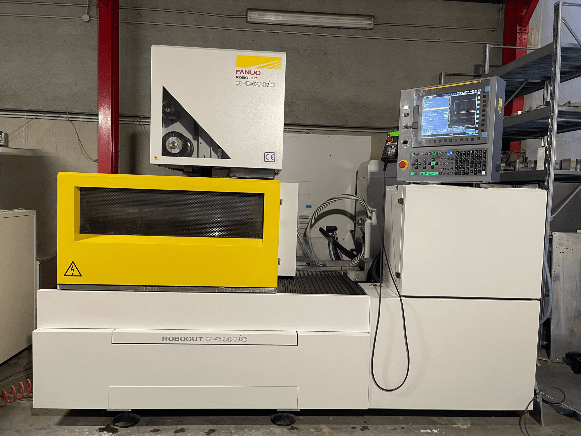 FANUC Robocut α-C600iC, vista lateral da máquina CNC com cobertura de segurança amarela e painel de controlo, apresentando a capacidade de corte de precisão.