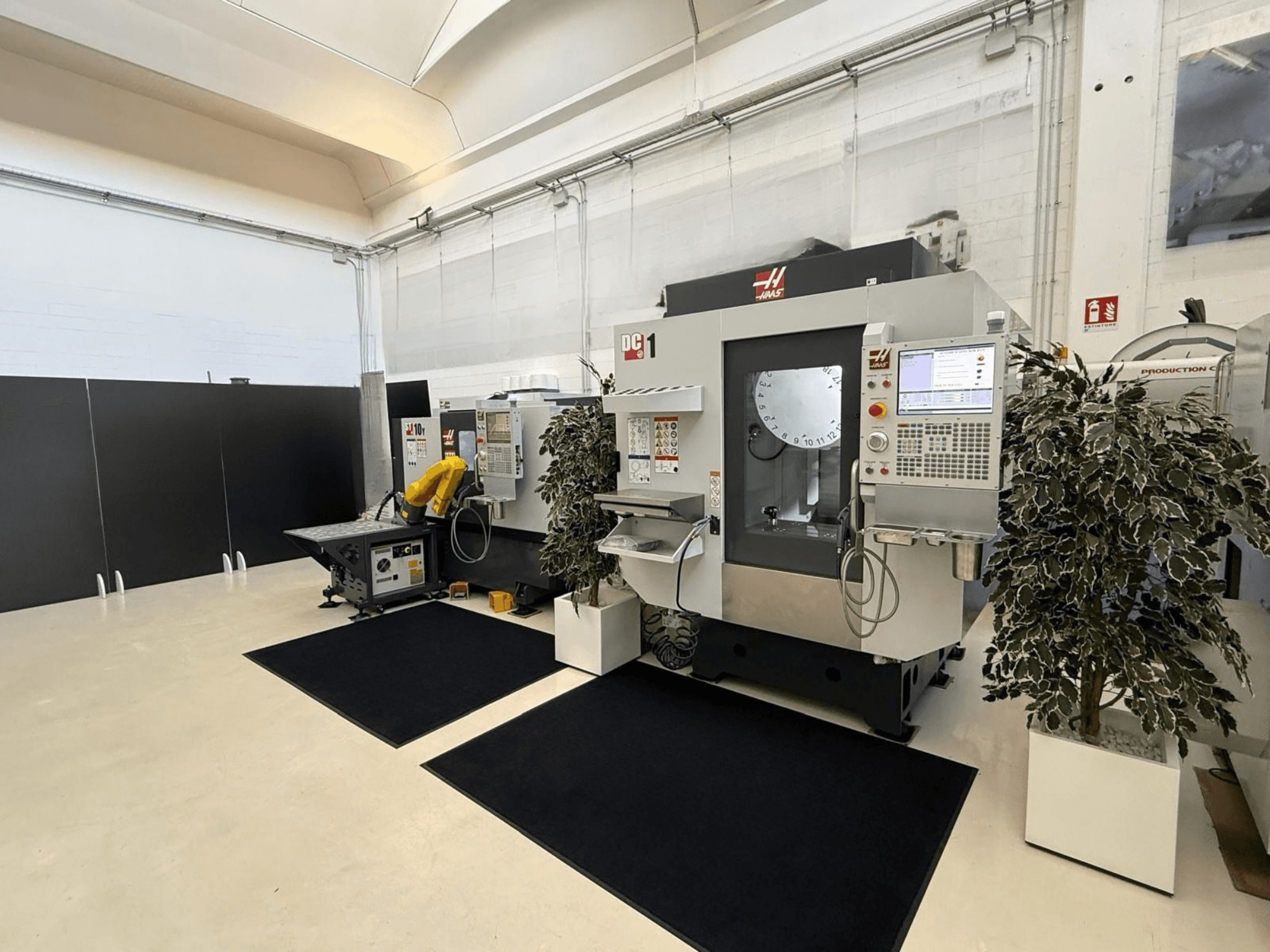 Vista frontal de um centro de maquinagem vertical HAAS DC-1 num espaço de trabalho limpo, com um painel de controlo tátil e as instalações circundantes.