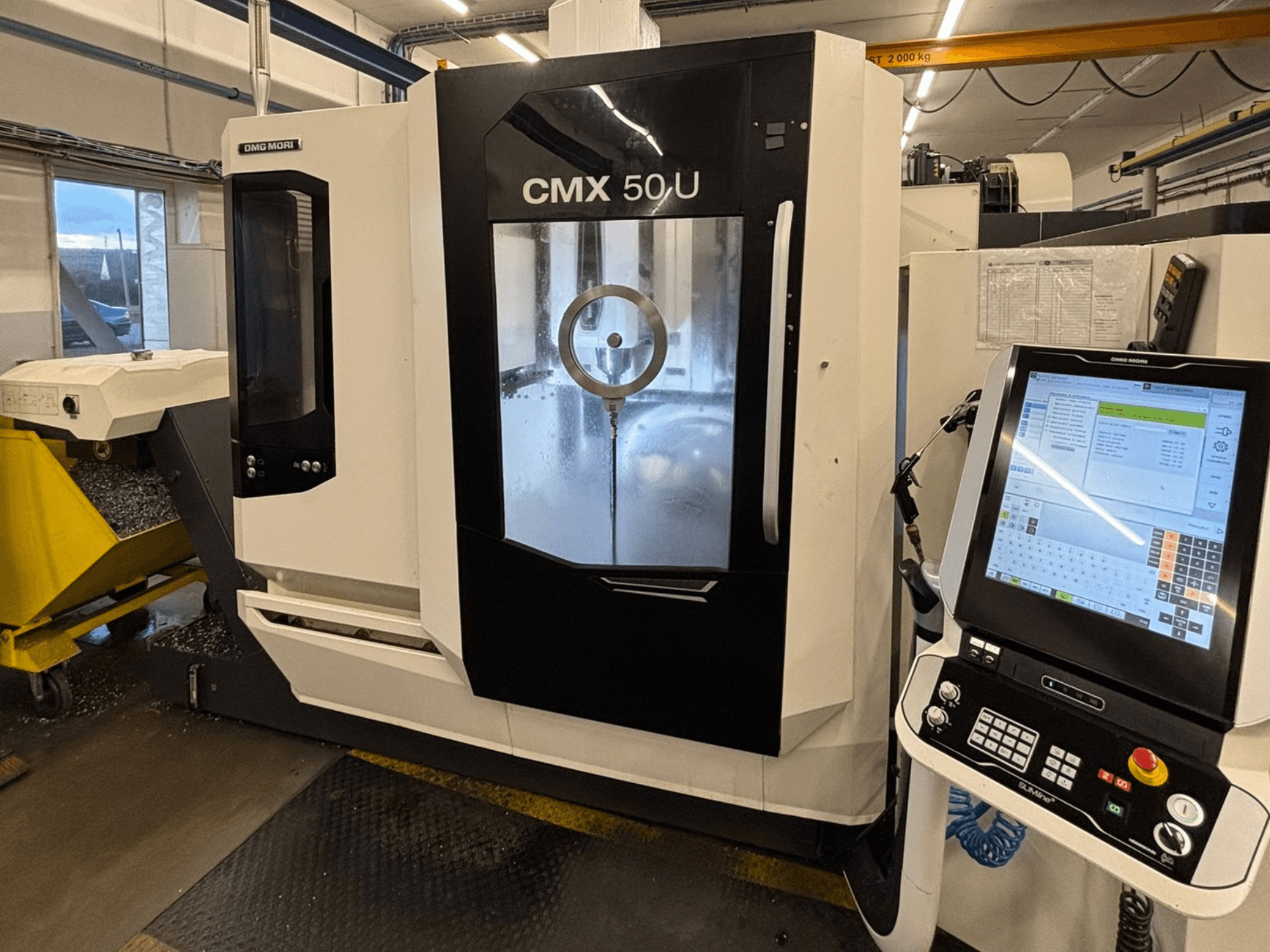 Centro de maquinação vertical DMG MORI CMX 50 U, vista frontal com painel de controlo e visor de vidro, mostrando a mecânica interna.