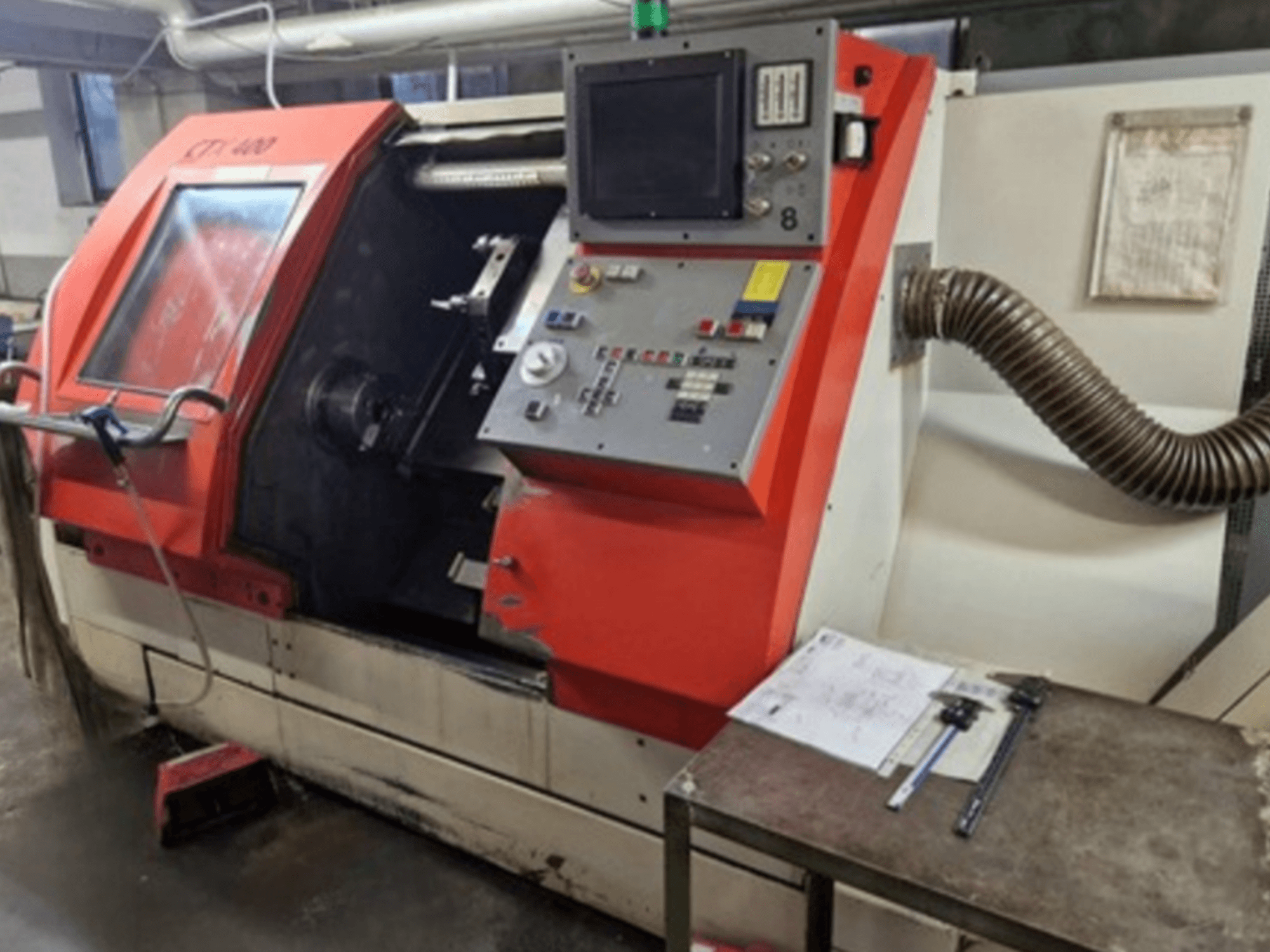 Gildemeister CTX 400 máquina de torneamento horizontal em vista frontal, mostrando o painel de controlo, a porta aberta e a mesa da oficina com ferramentas.