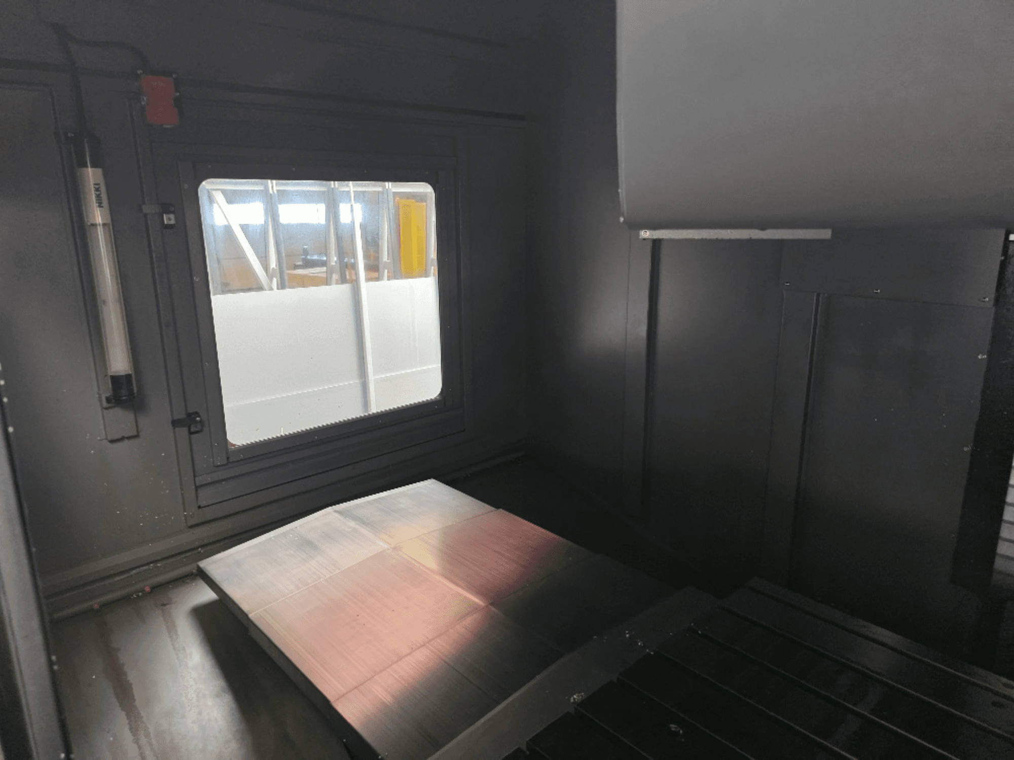 Vista interior de uma caixa de máquina com uma placa de metal polido, uma janela lateral e iluminação mínima. Nenhuma marca visível.