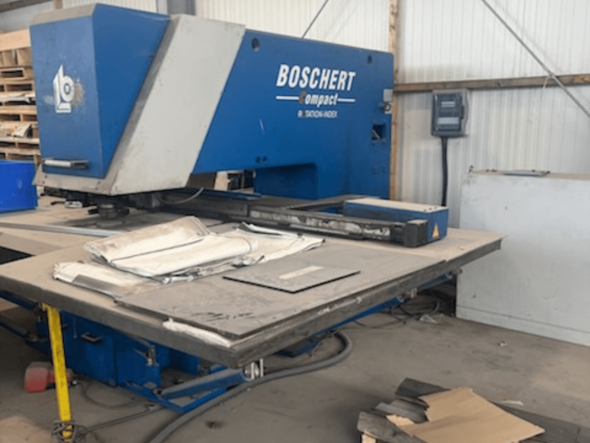 Máquina de perfuração CNC BOSCHERT COMPACT 1000 numa oficina, mostrando a vista frontal com chapas metálicas na mesa.