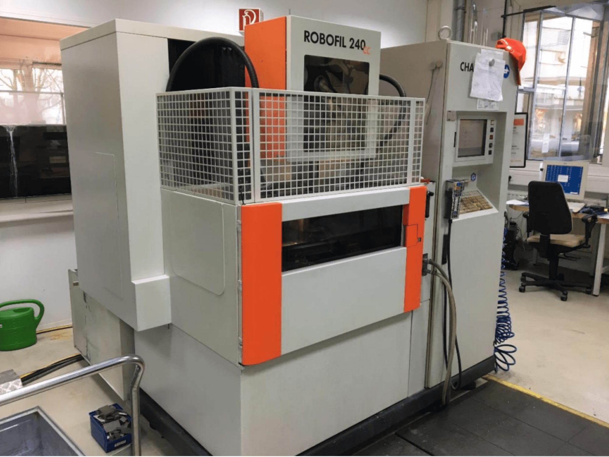 Vista frontal da máquina de eletroerosão por fio CHARMILLES ROBOFIL 240 CC, com uma grelha de proteção e um painel de controlo, localizada numa oficina.