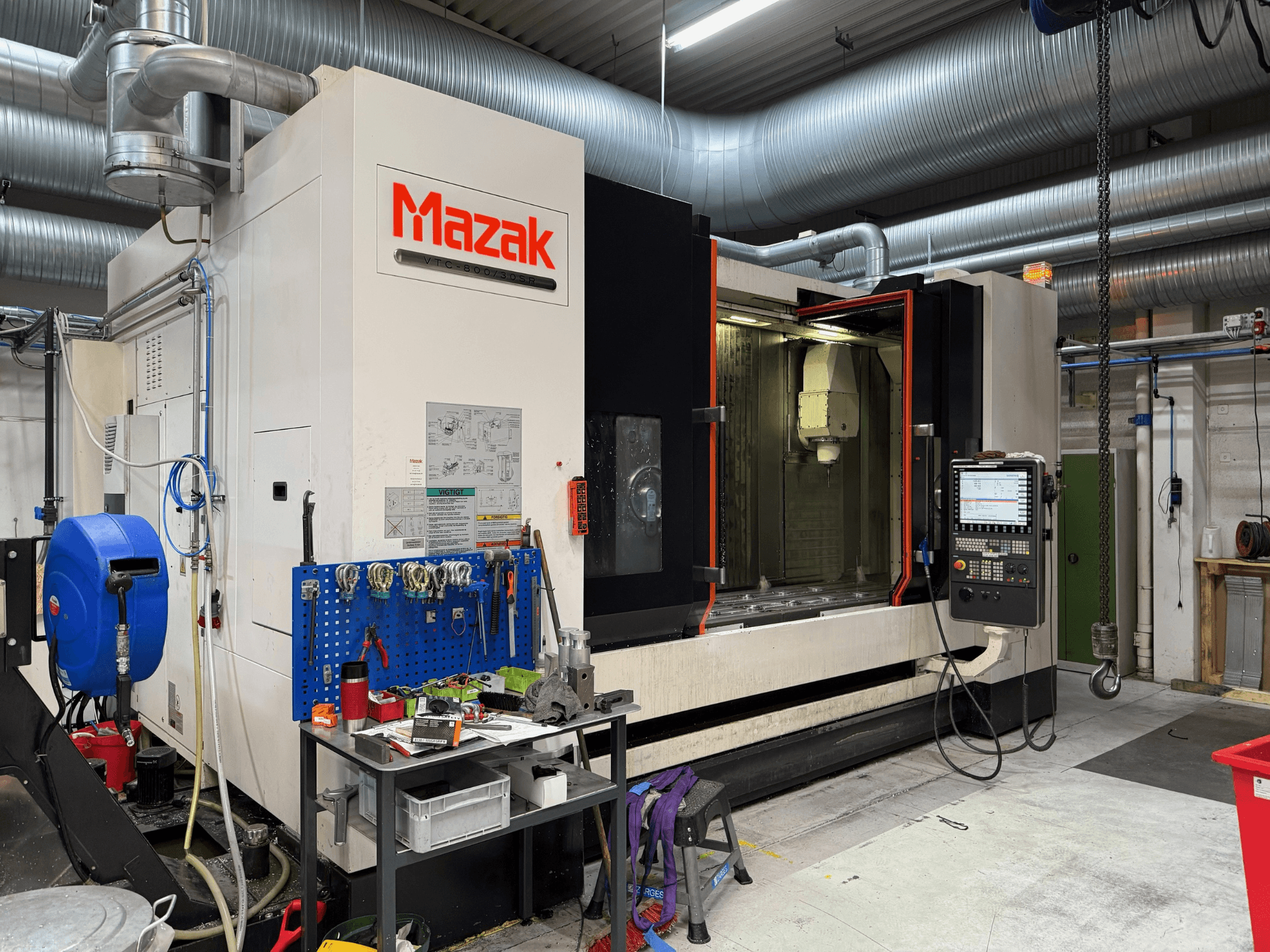 Máquina CNC Mazak numa vista frontal, com controlos, ferramentas e espaço de trabalho num ambiente de maquinação.