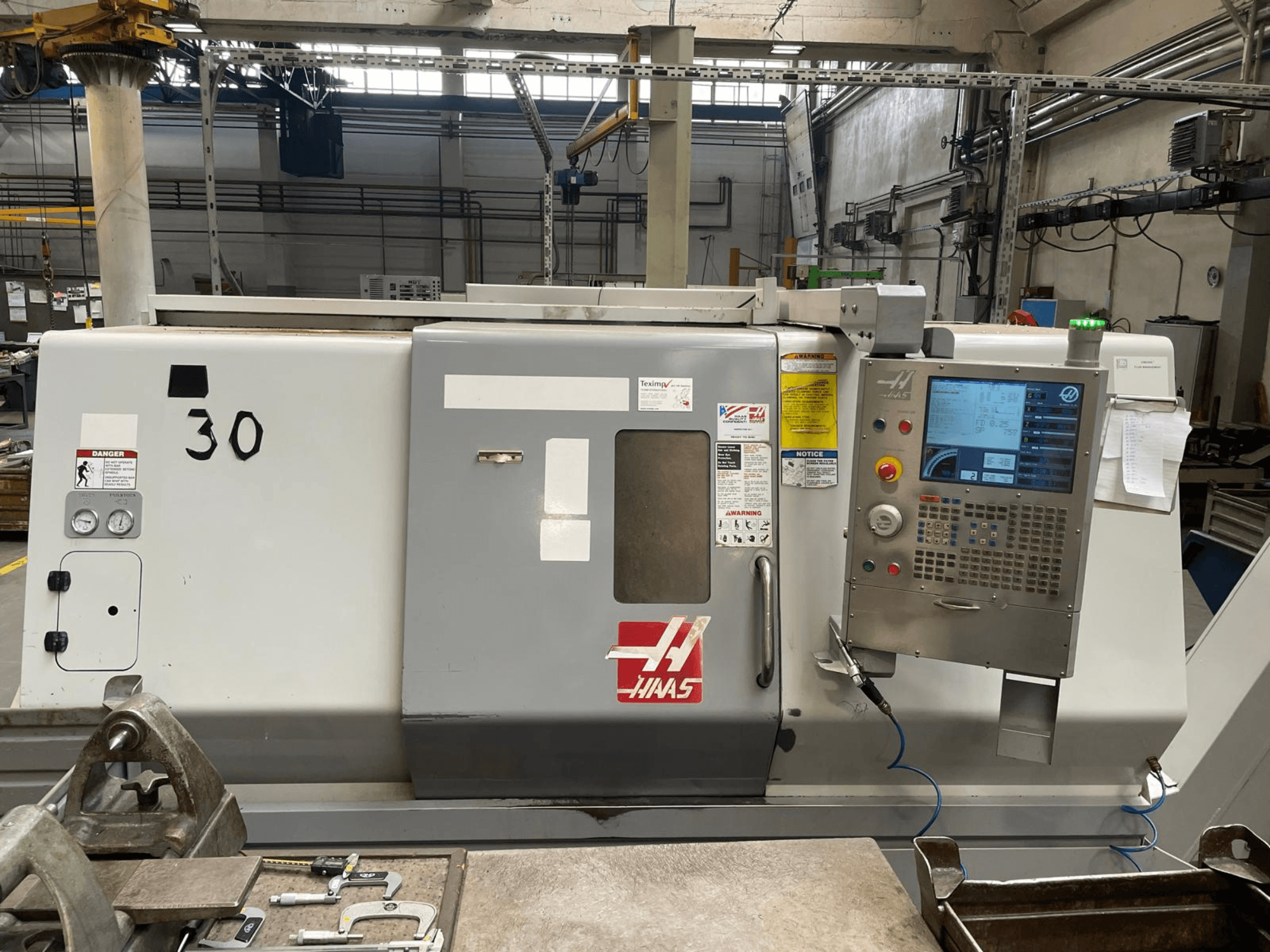 Vista frontal do torno horizontal Haas SL-30THE, com painel de controlo digital, etiquetas de aviso de perigo e o número de modelo 30.