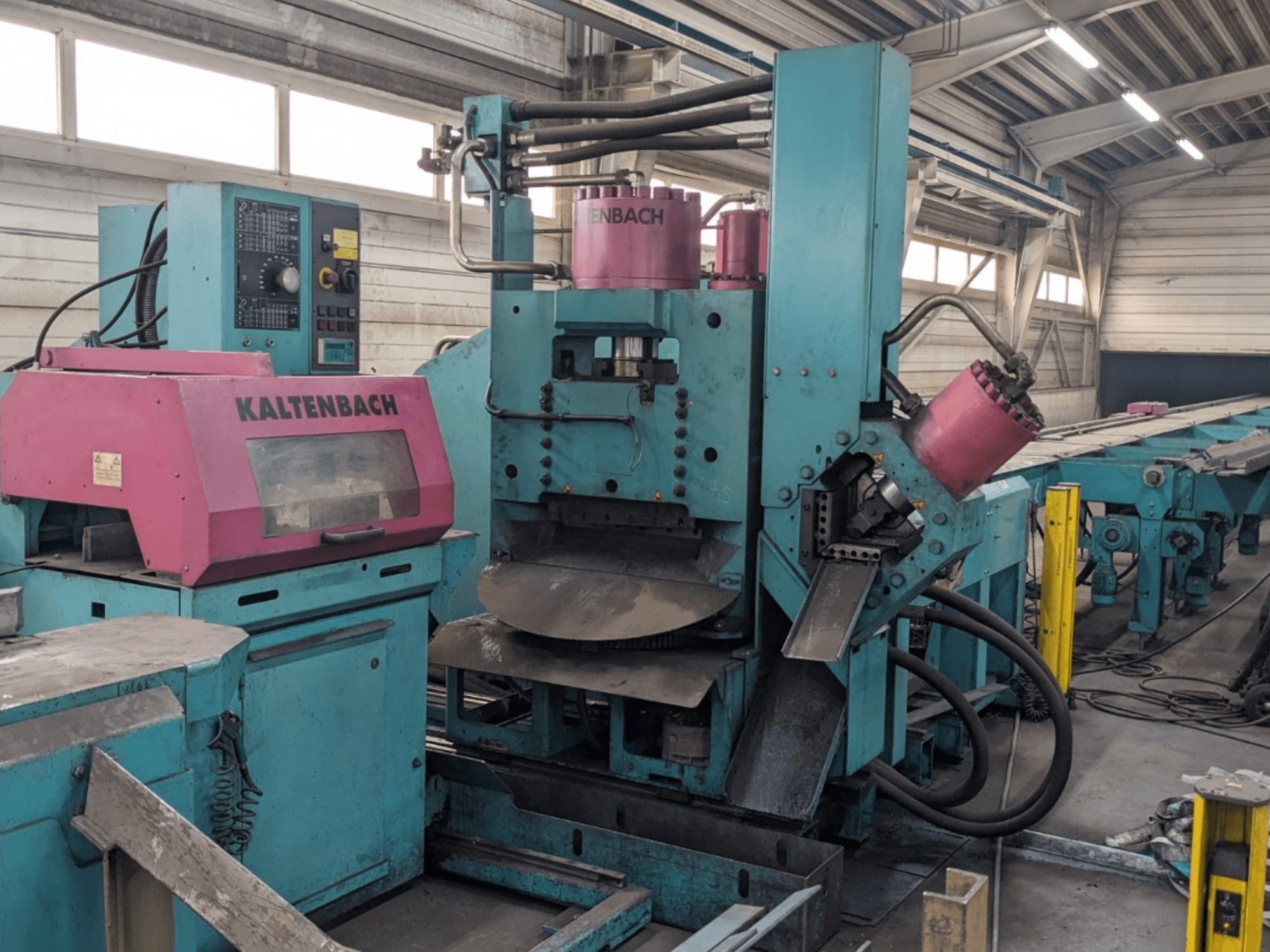 Máquina industrial KALTENBACH em azul-petróleo e rosa, vista de frente, com painel de controlo e componentes hidráulicos.