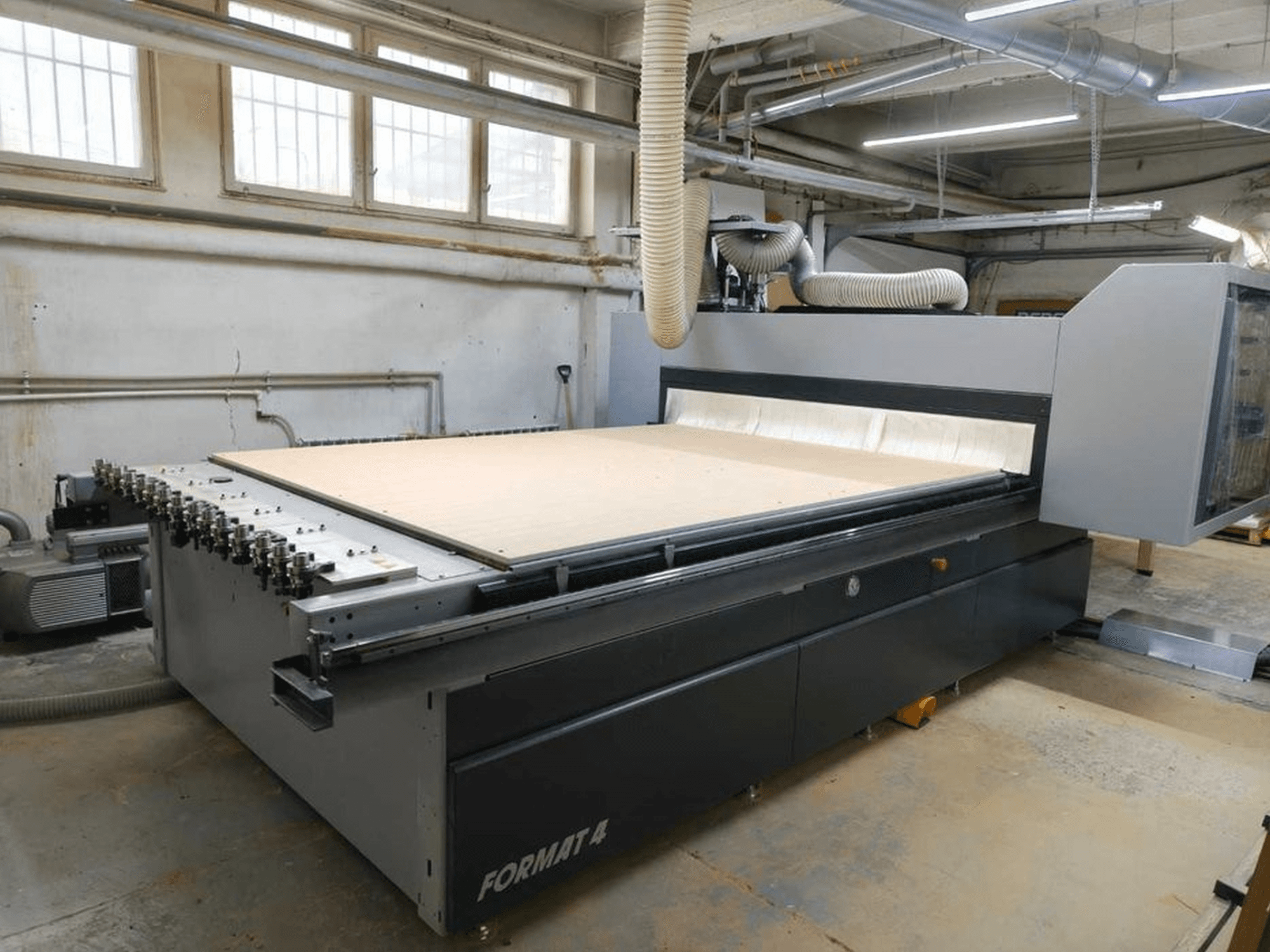 CNC Router FORMAT4 Profit H80 21.31 na oficina, vista lateral com uma grande superfície de corte e mangueira visível para extração de poeiras.