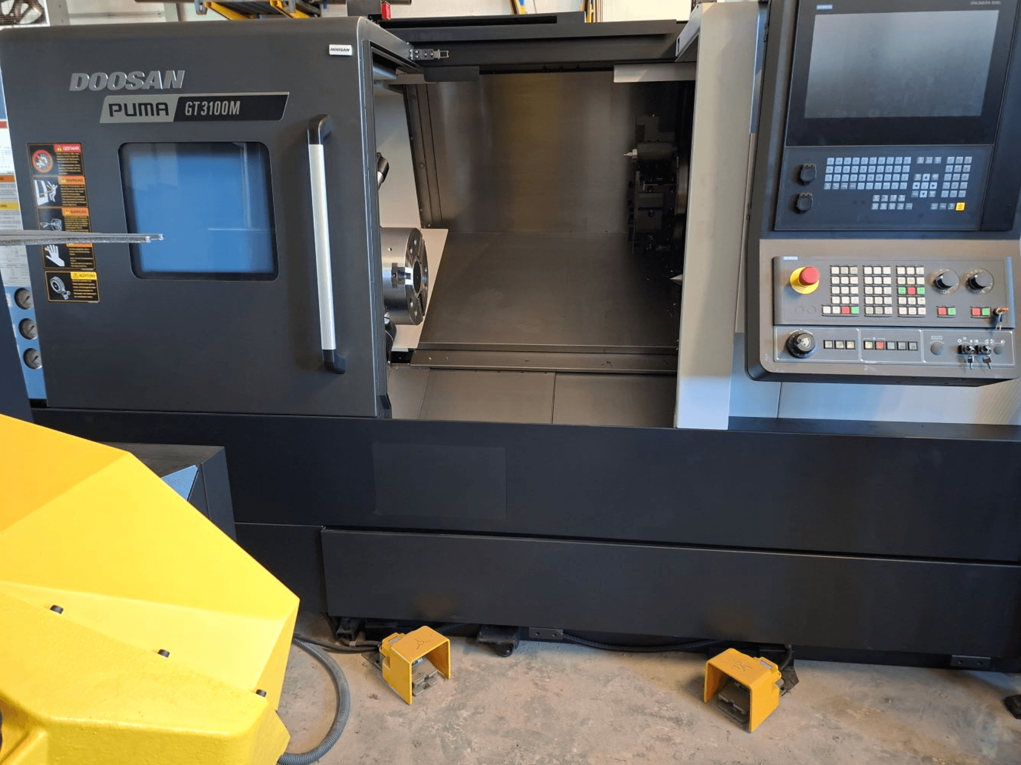 DOOSAN Puma GT 3100 M, torneiro horizontal em vista frontal, mostrando o painel de controlo, a torre aberta e o espaço de trabalho interior.