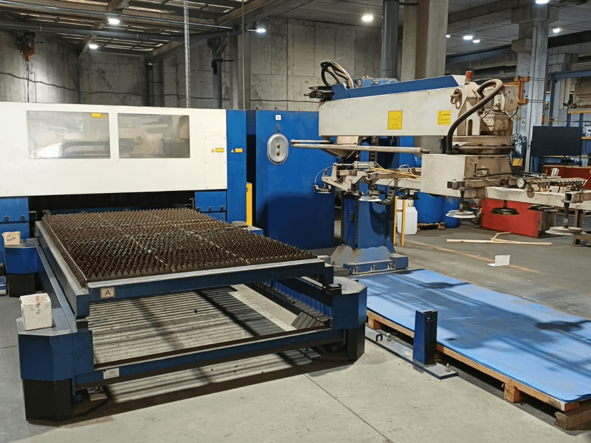 Máquina de corte a laser de CO₂ TRUMPF TRUMATIC L 3030, vista lateral, mostrando a mesa de corte com superfície estriada e o braço robótico.