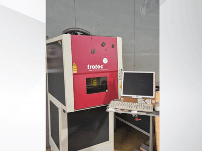Estação de trabalho a laser Trotec vermelha, vista de frente, com um monitor e um teclado numa estação de trabalho.
