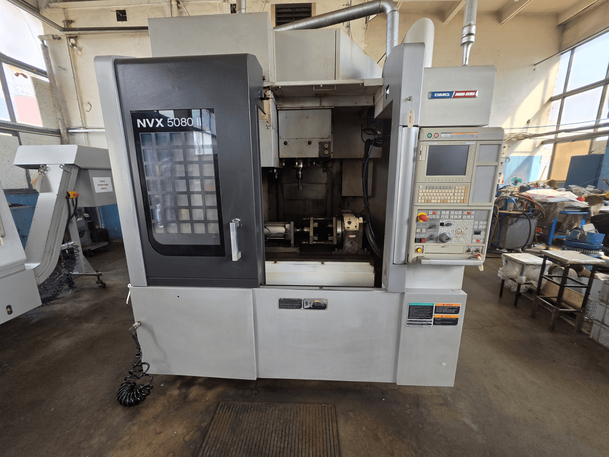 Vista frontal do centro de maquinagem vertical DMG Mori Seiki NVX 5080 II/40, com painel de controlo e janela transparente, que permite visualizar a área de maquinagem.