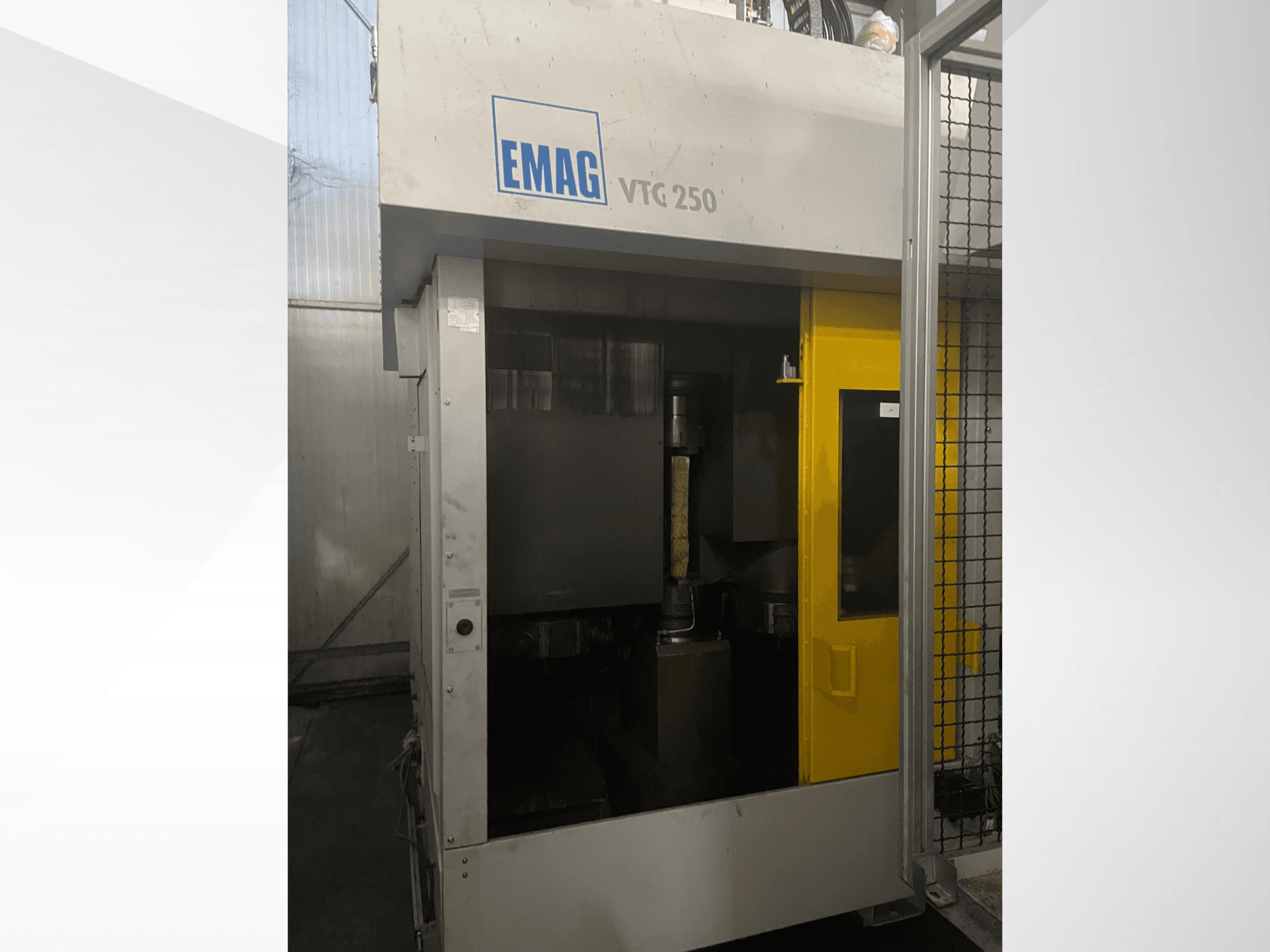 Centro de maquinação vertical EMAG VTC 250 em vista frontal, com uma porta amarela e uma ferramenta de corte visível no interior da câmara.