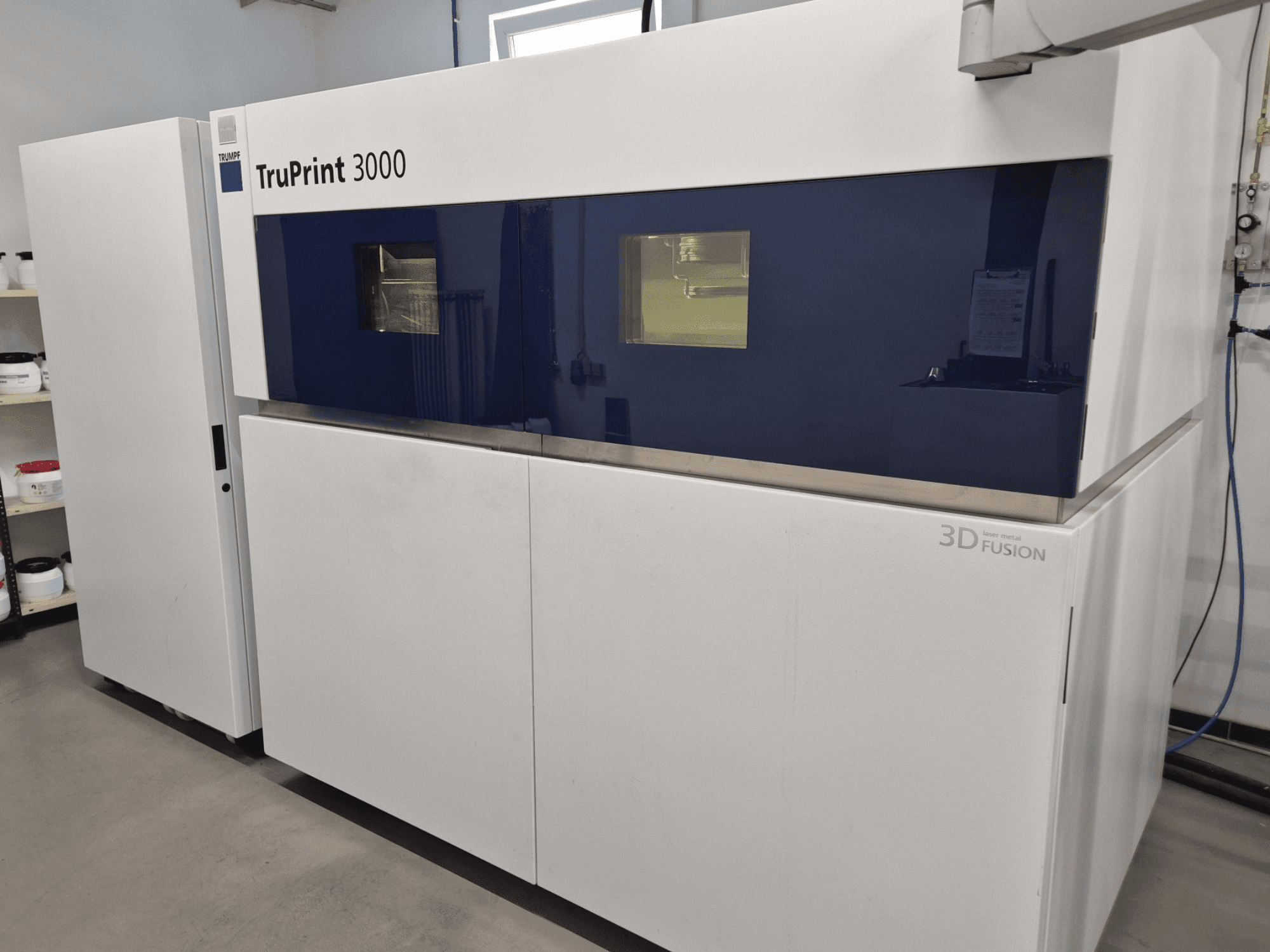 Impressora 3D de metal TruPrint 3000 em vista frontal, com design de painel azul e tecnologia de fusão a laser.