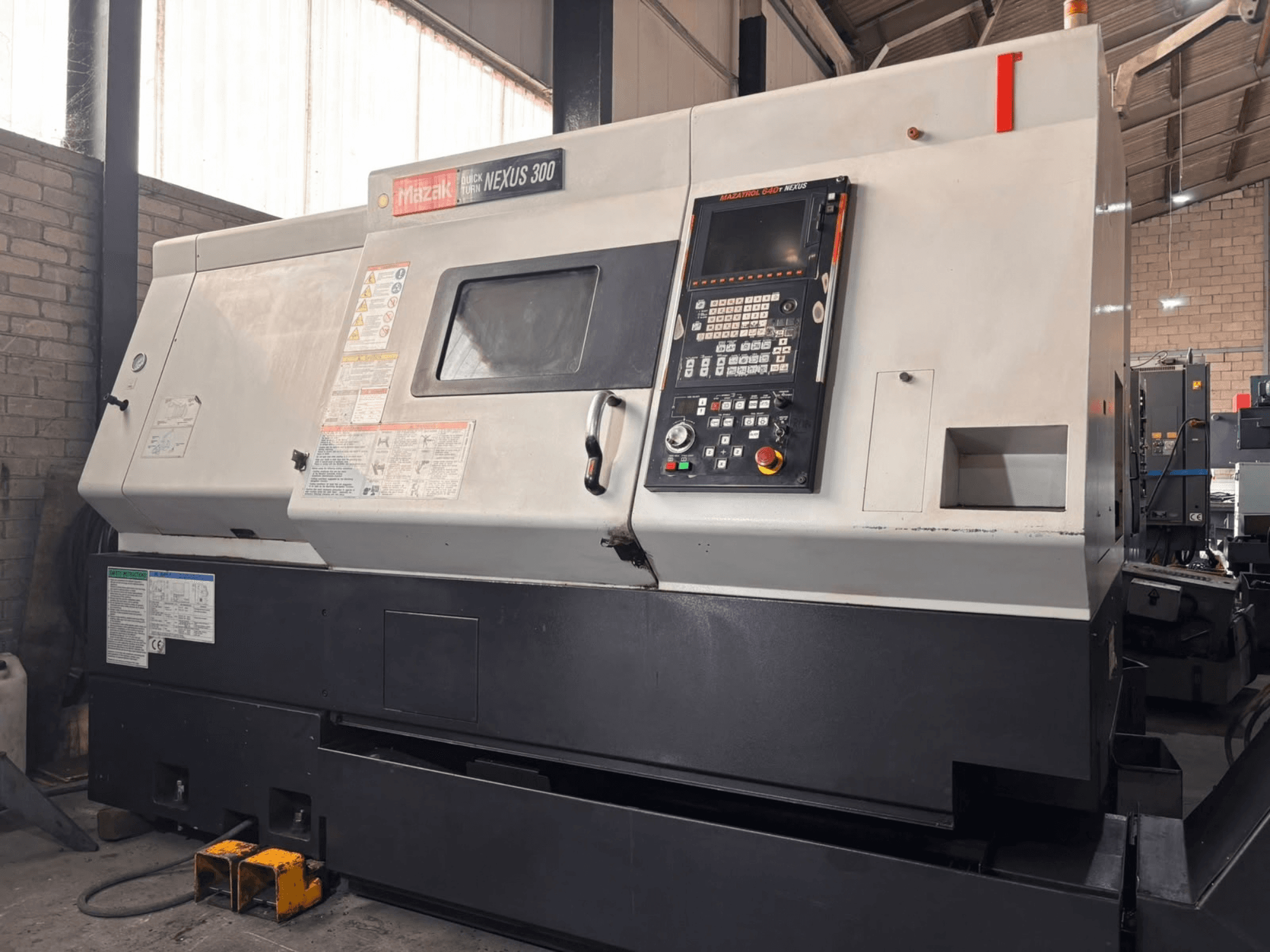 Torno horizontal Mazak QT NEXUS 300, vista lateral que mostra o painel de controlo e os indicadores de funcionamento num ambiente de oficina.