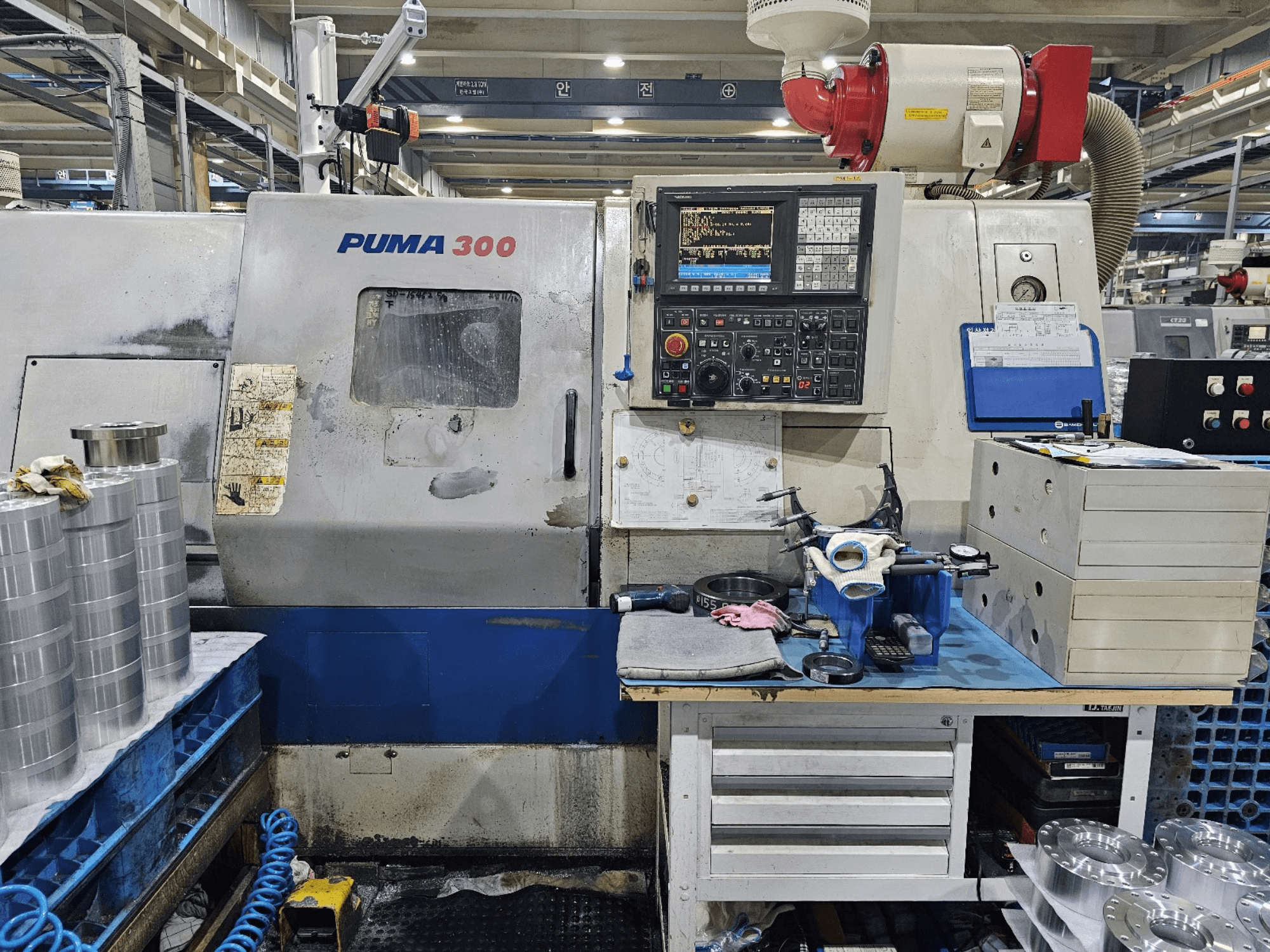 Máquina CNC PUMA 300 numa oficina; vista frontal mostrando o painel de controlo, ferramentas e peças metálicas numa bancada de trabalho.