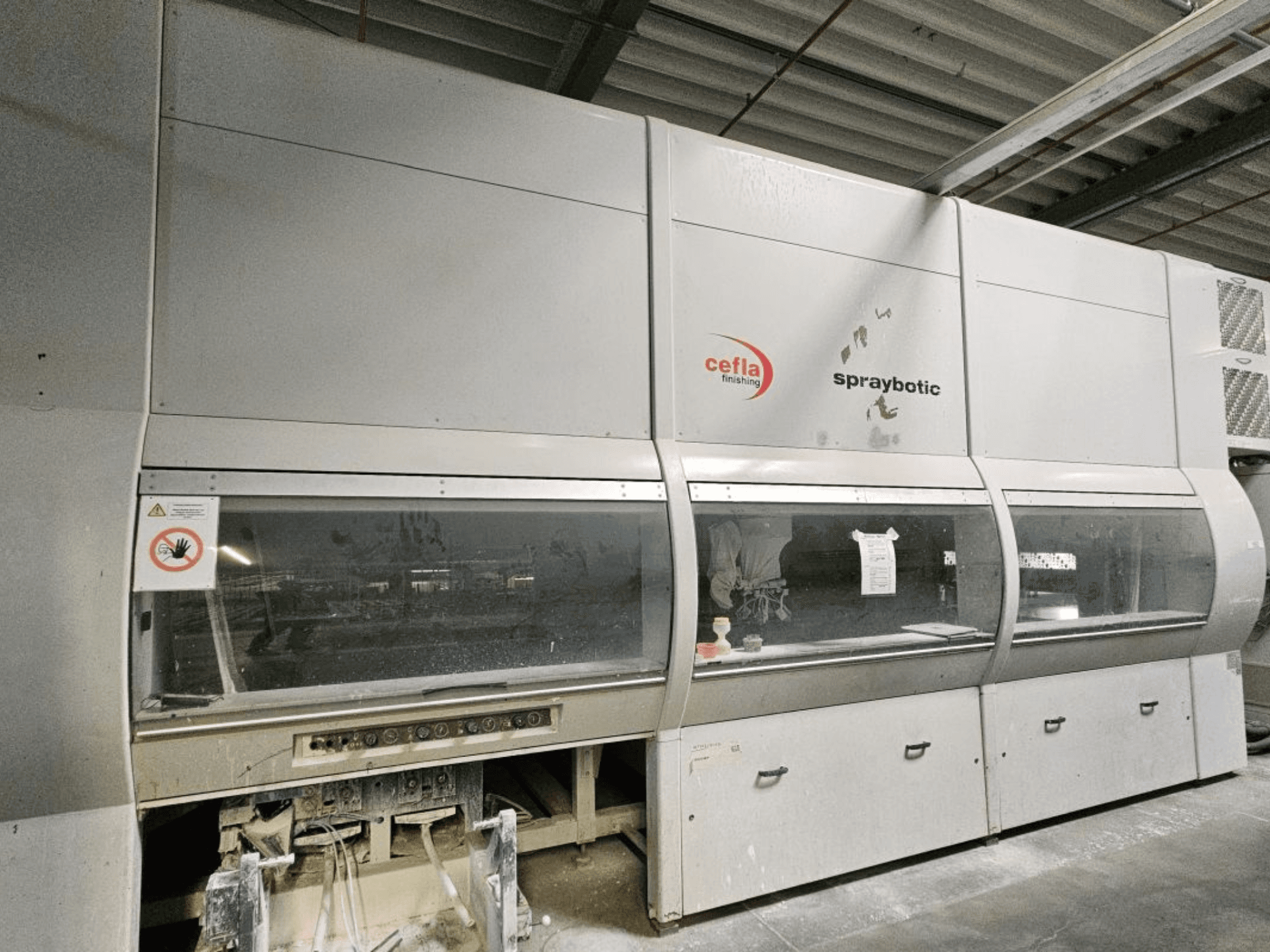Linha de produção Cefla Spraybotic MD para madeira, vista frontal, mostrando o painel de controlo e as janelas de visualização transparentes.