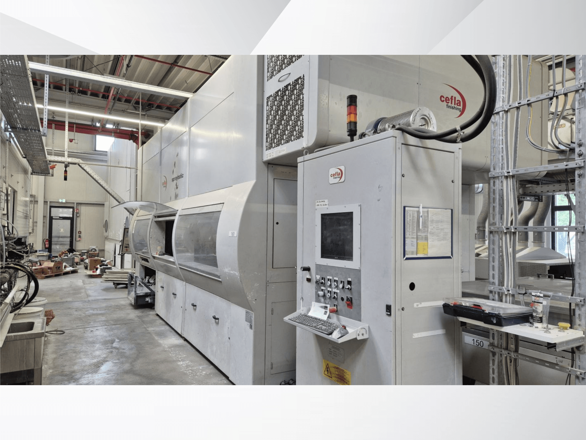 Linha de produção Cefla Spraybotic MD numa oficina, vista frontal que mostra o painel de controlo e a câmara de pulverização com tampa transparente.