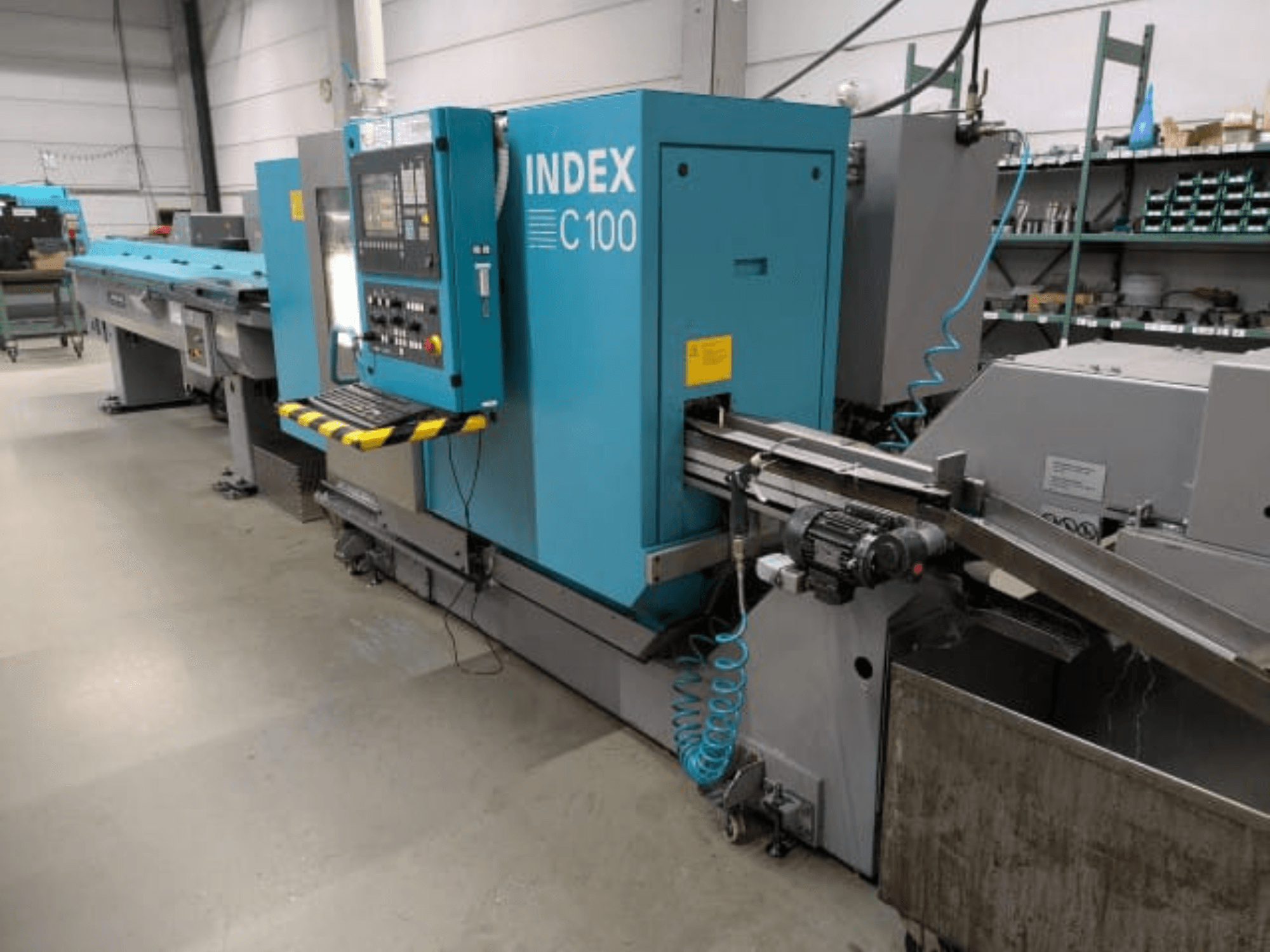 Torno horizontal Index C100, vista lateral; inclui um painel de controlo, um sistema de avanço e um recipiente de recolha de aparas de metal.