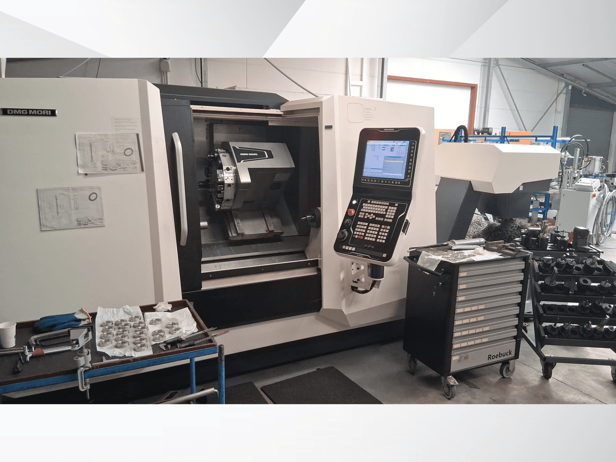 Torneiro horizontal DMG MORI CLX450 em vista frontal, com painel de controlo, área de trabalho, ferramentas e peças metálicas.