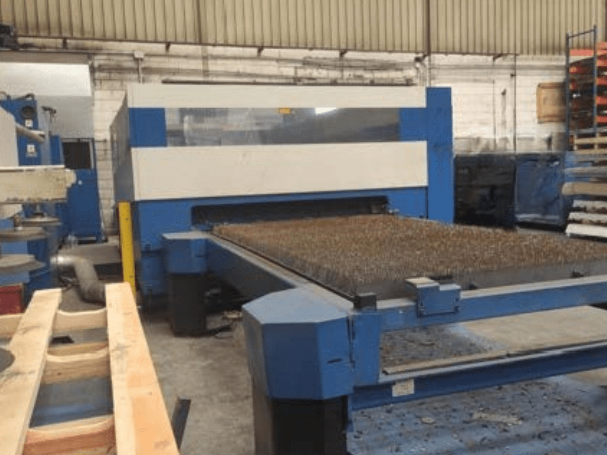Máquina de corte a laser azul com uma base de metal texturizado, vista lateral, mostrando a configuração operacional num espaço de trabalho industrial.