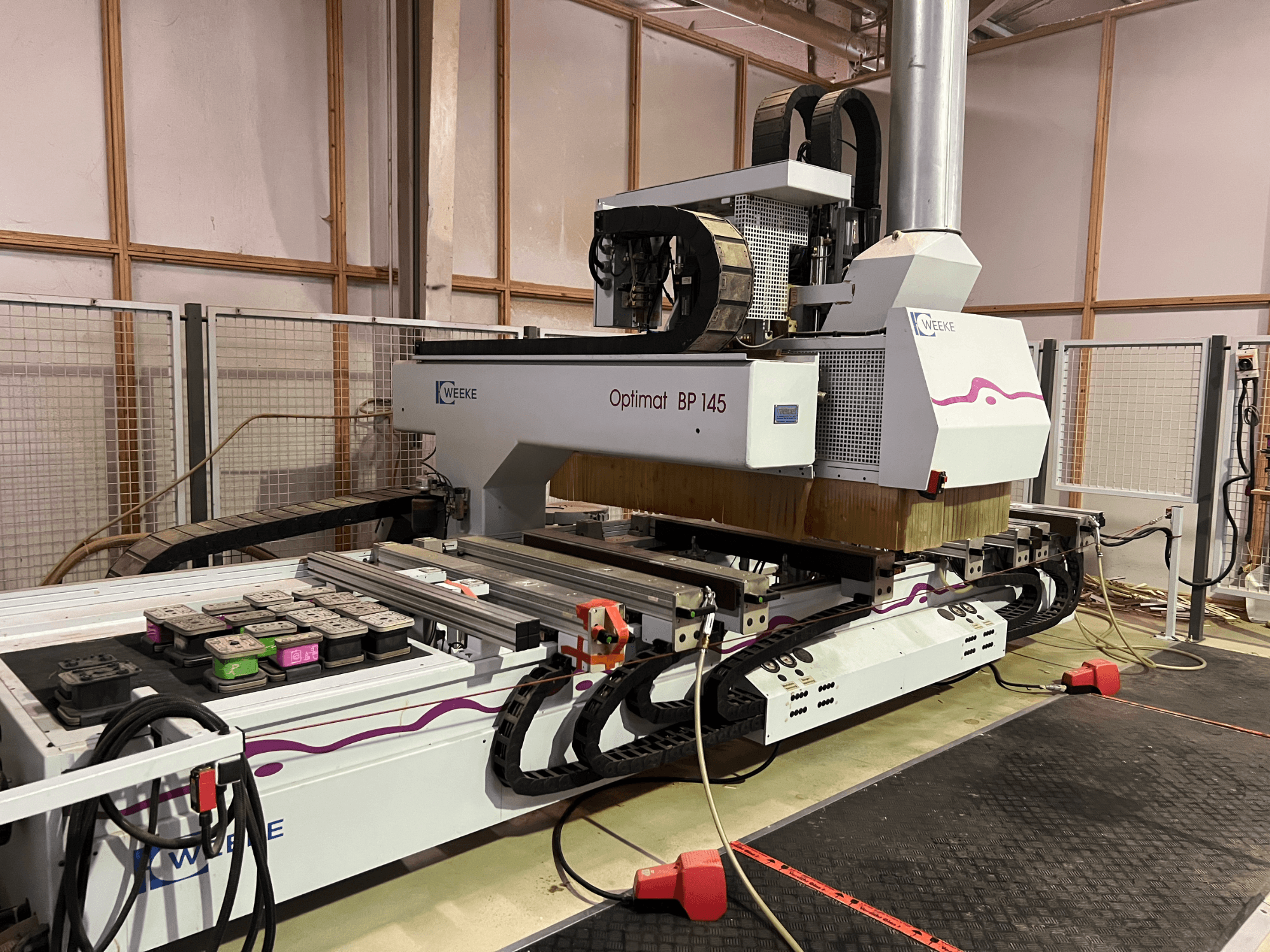 WEEKE Optimat BP 145 numa fábrica, mostrando uma máquina CNC com botões e cabos de controlo, vista de lado.