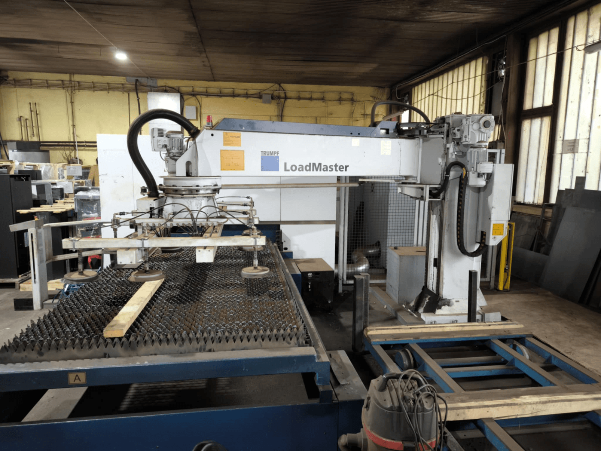 Máquina de corte TRUMPF TRULASER 3030 FIBER, vista frontal, mostrando o sistema LoadMaster e posicionada numa mesa de trabalho gradeada.
