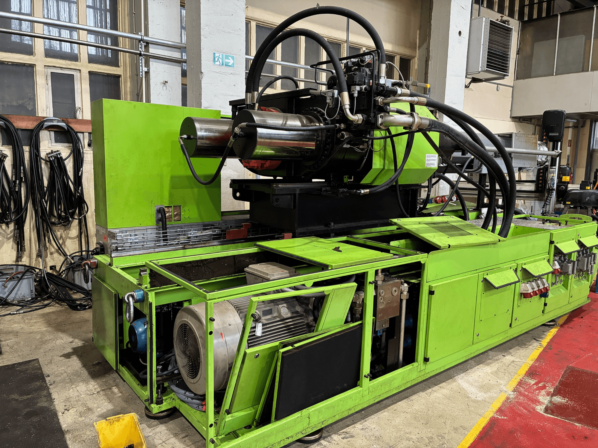 Máquina industrial verde com sistema hidráulico, vista frontal, mostrando o motor e vários painéis de controlo.
