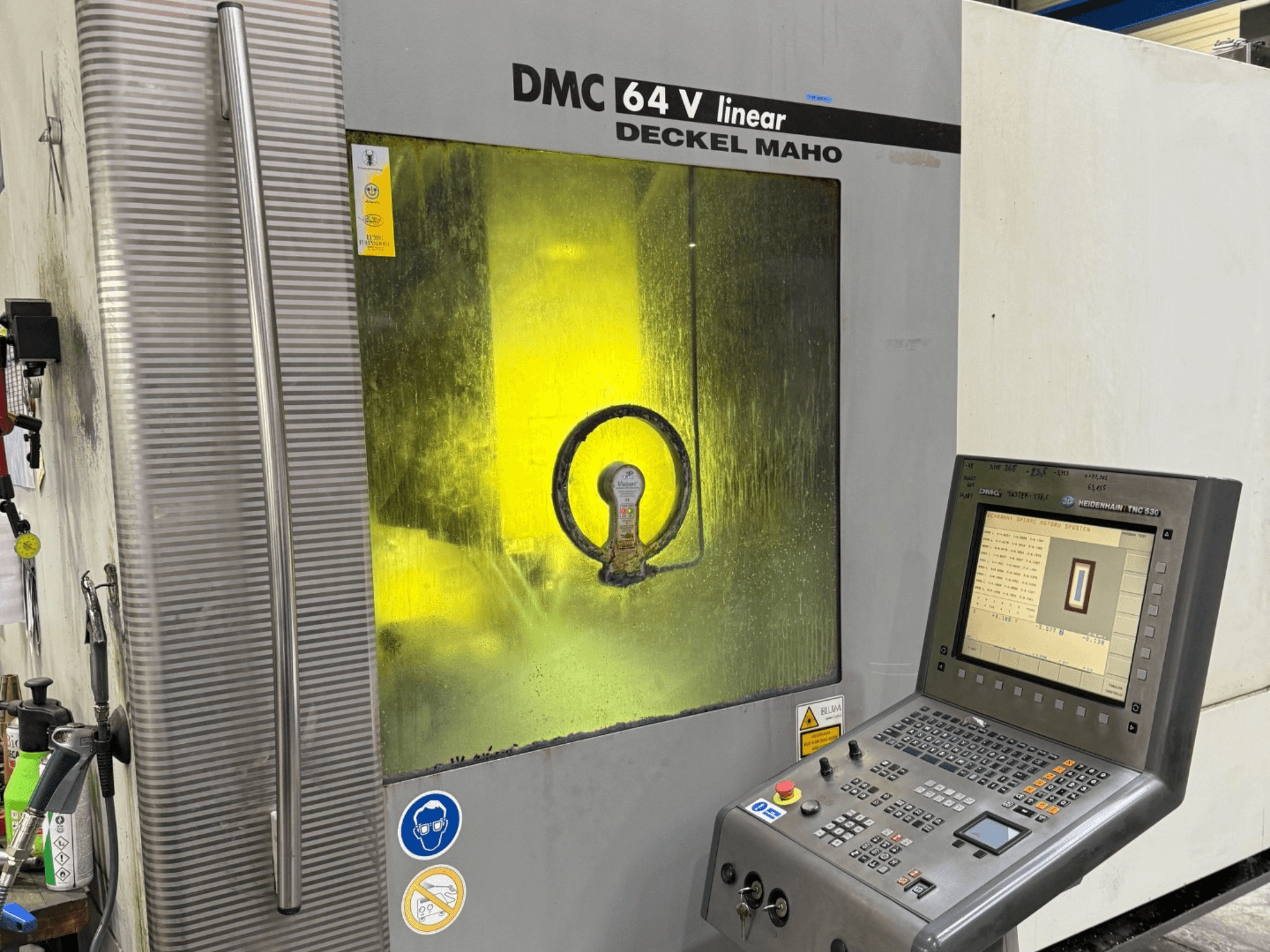 DMC 64 V linear de Deckel Maho, vista frontal da máquina com painel de controlo e janela amarela que mostra os mecanismos internos.
