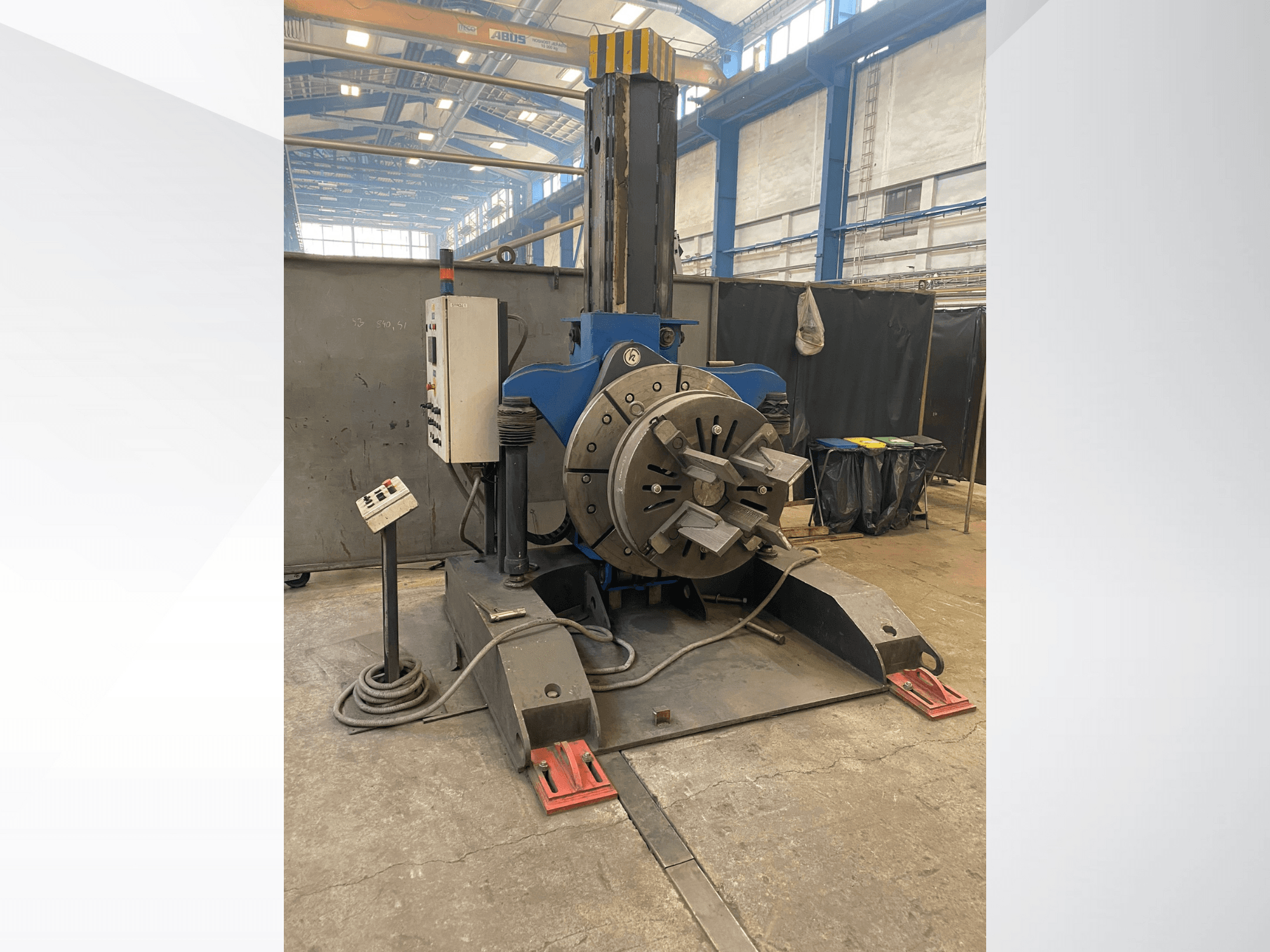 Torno industrial azul com cabeça rotativa redonda e painel de controlo, vista lateral, numa oficina.