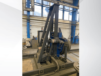 Máquina industrial com motor azul e estrutura metálica, vista de frente numa oficina.