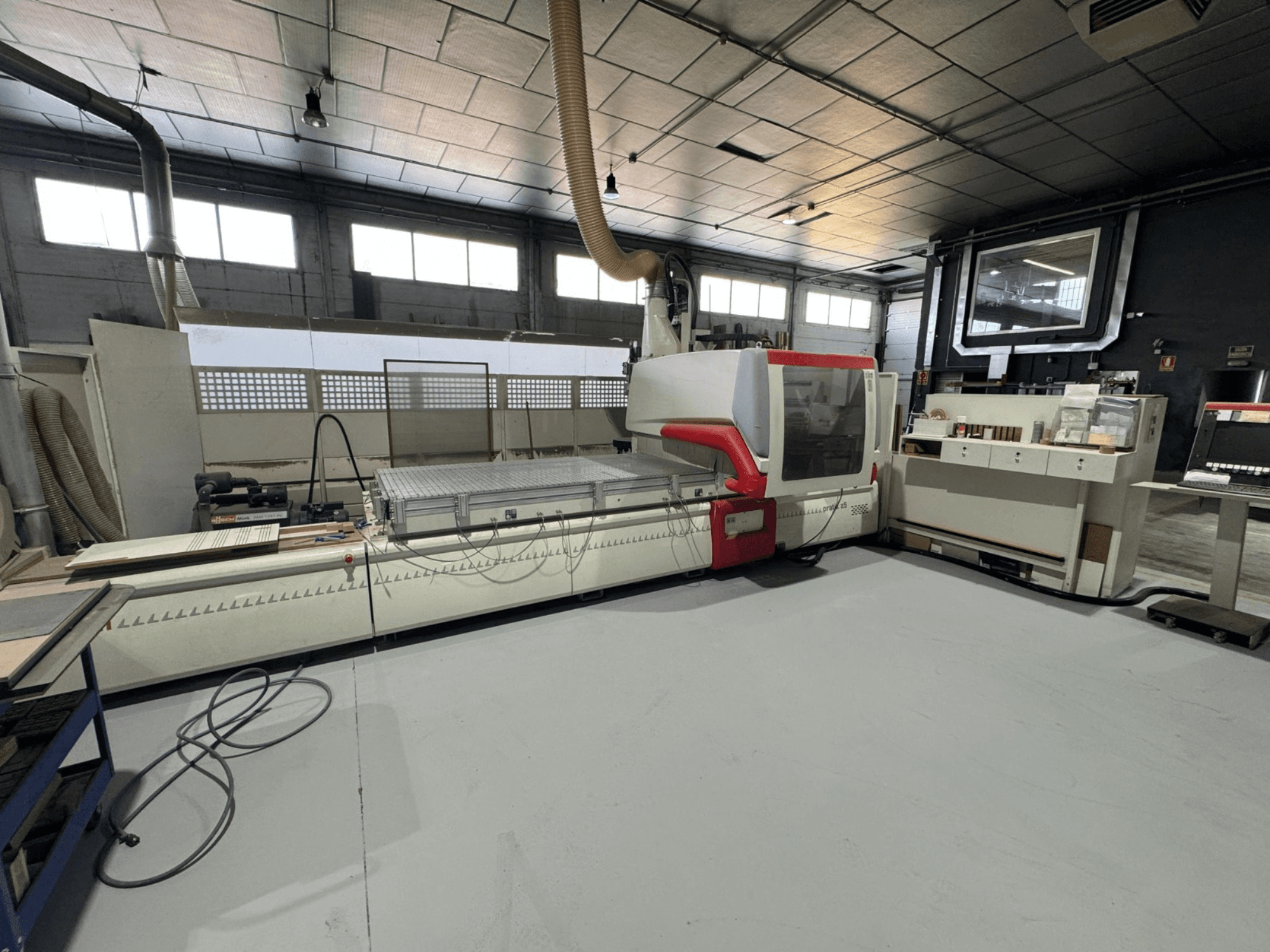 Máquina CNC numa oficina, vista de frente com detalhes em vermelho, equipada com painel de controlo e superfície de trabalho, para corte de precisão.