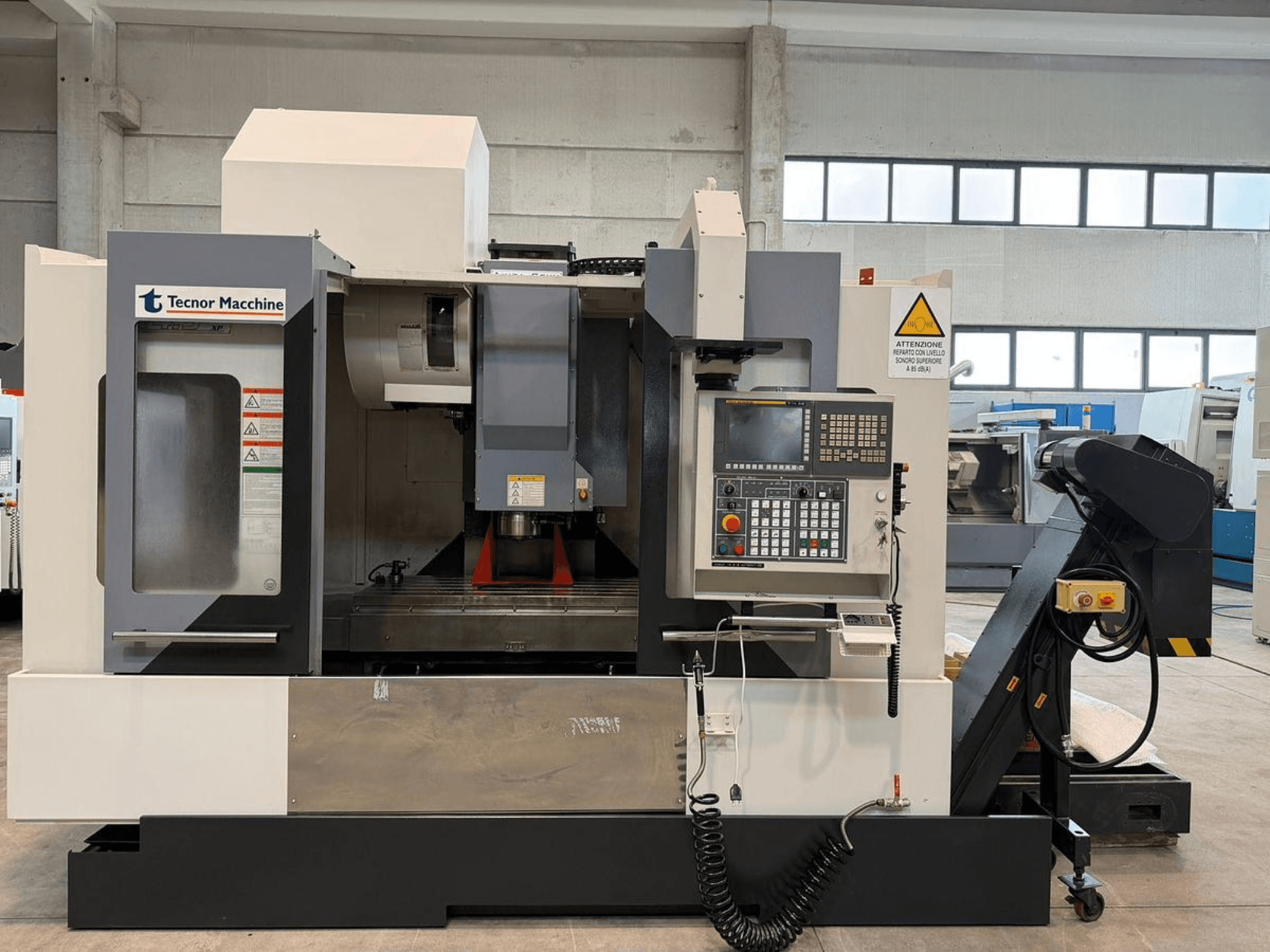 Fresadora CNC Tecnor Machine, vista frontal, com painel de controlo com botões, etiquetas de aviso e suporte de ferramentas.