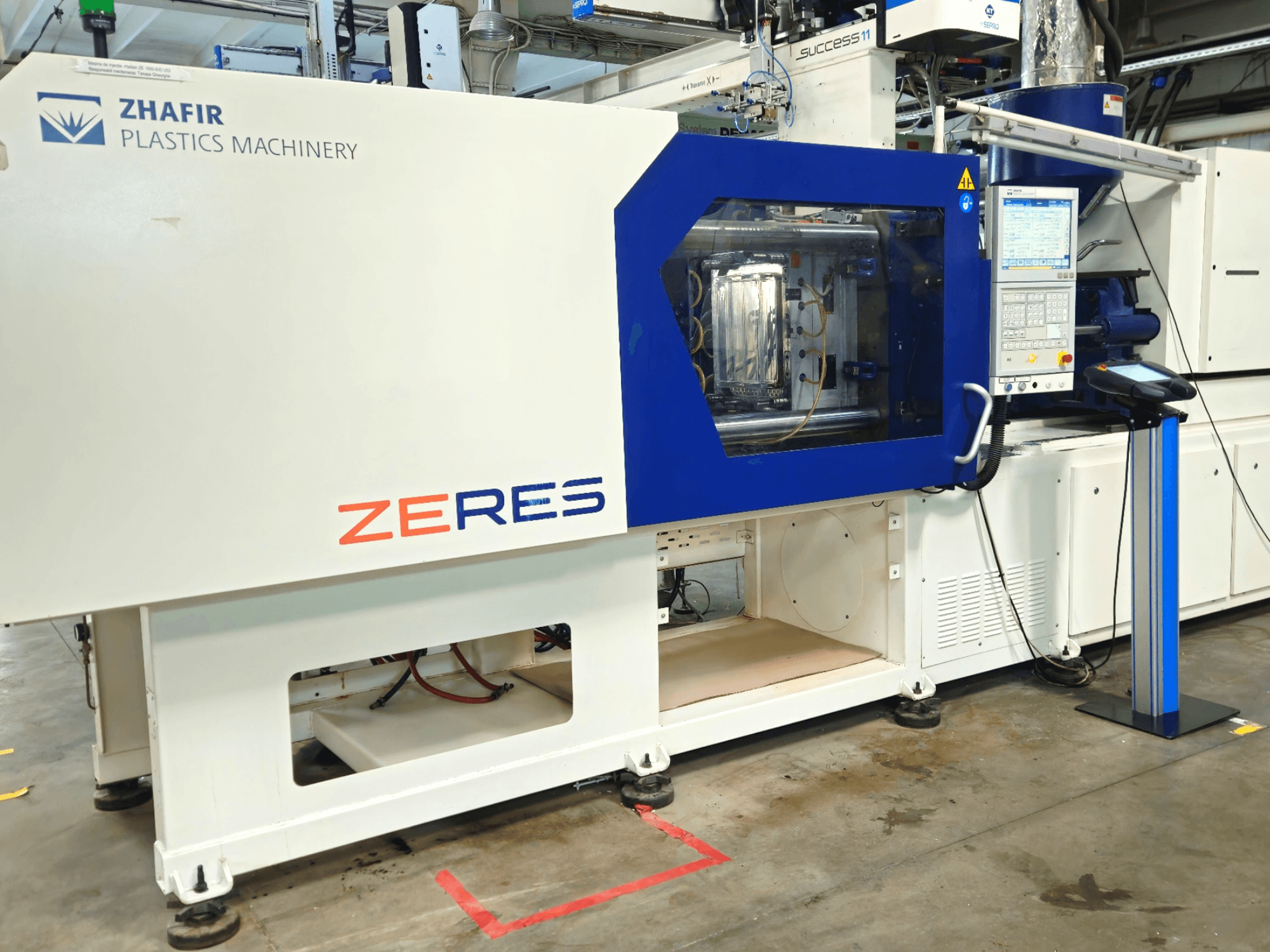 Máquina de moldagem por injeção Zhafir Zeres em vista frontal, com painel de controlo e área de moldagem transparente.