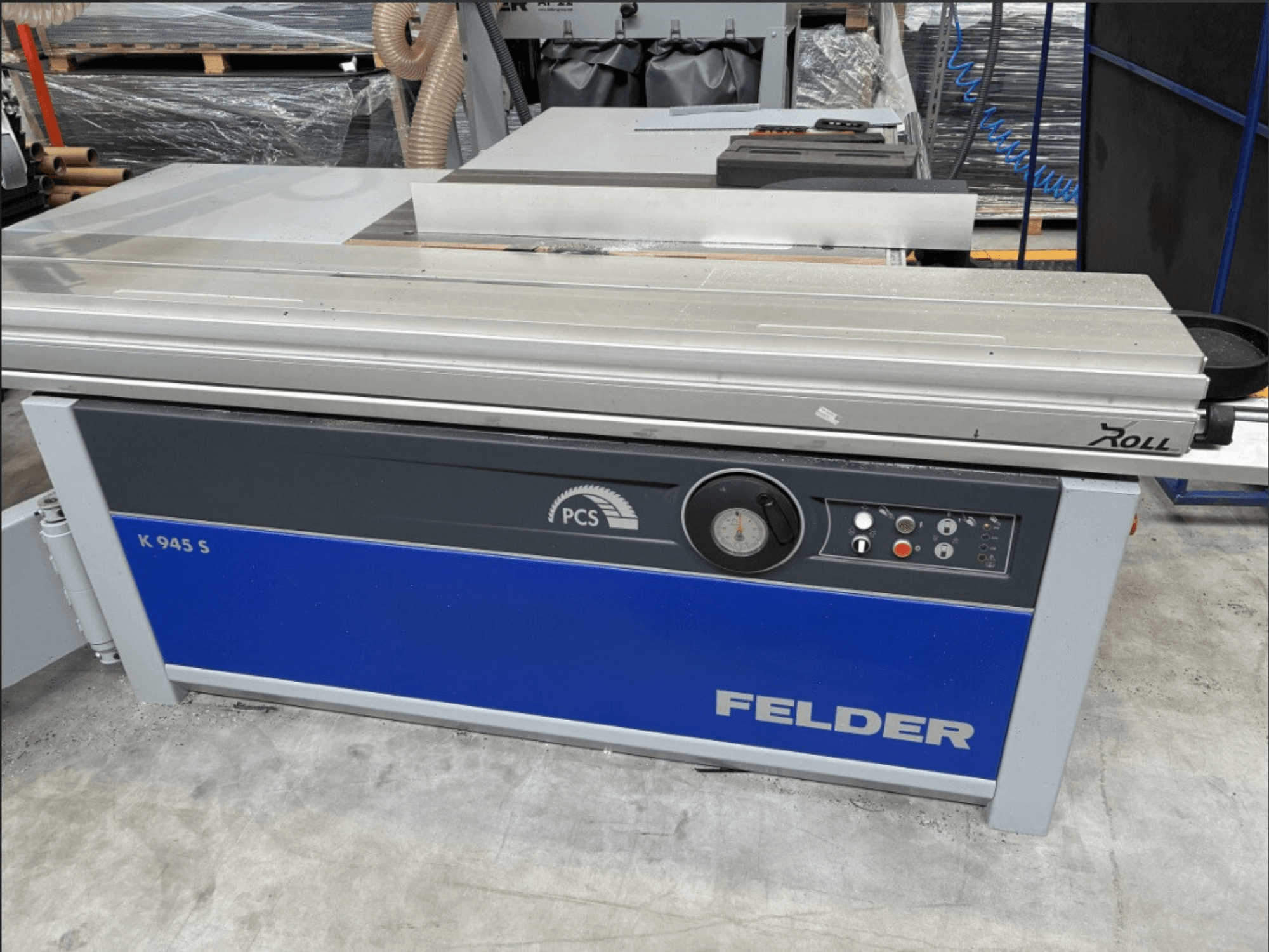 Serra de painéis FELDER K 945 S, vista frontal mostrando o painel de controlo, a mesa e os dispositivos de segurança, instalada no chão de uma oficina.
