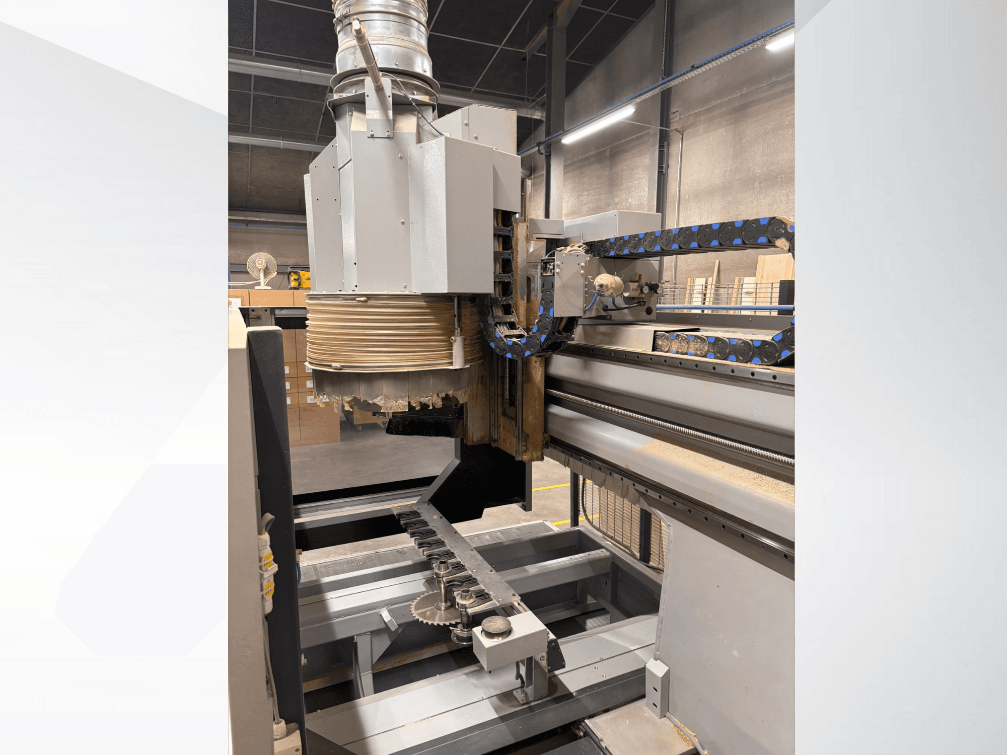 Máquina de fresar CNC com um fuso grande e um transportador, vista lateral, com ferramentas de corte de madeira e componentes de máquinas.