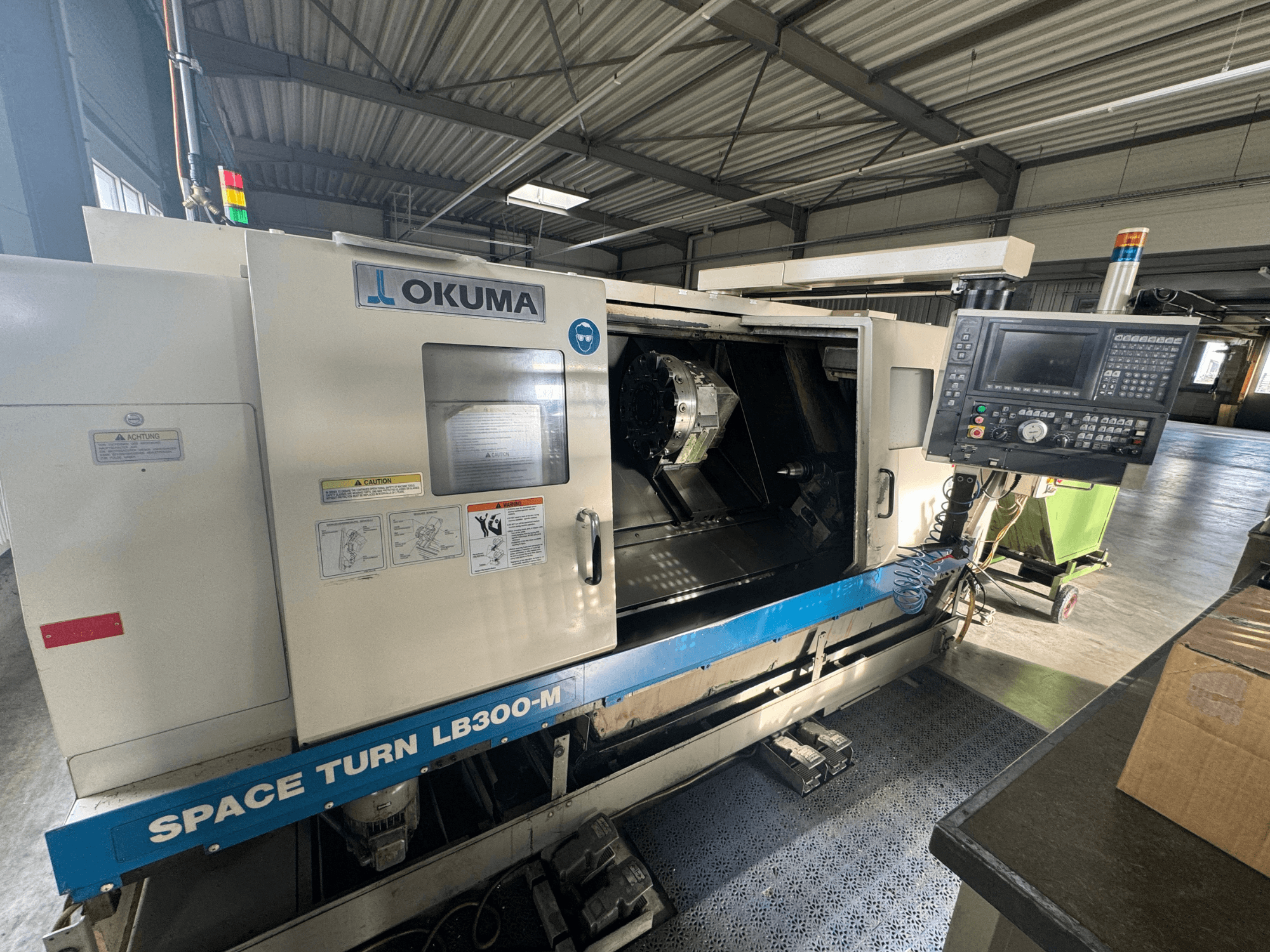 Torno CNC Okuma Space Turn LB300-M em vista frontal, com painel de controlo e porta aberta revelando a área de maquinação interior.