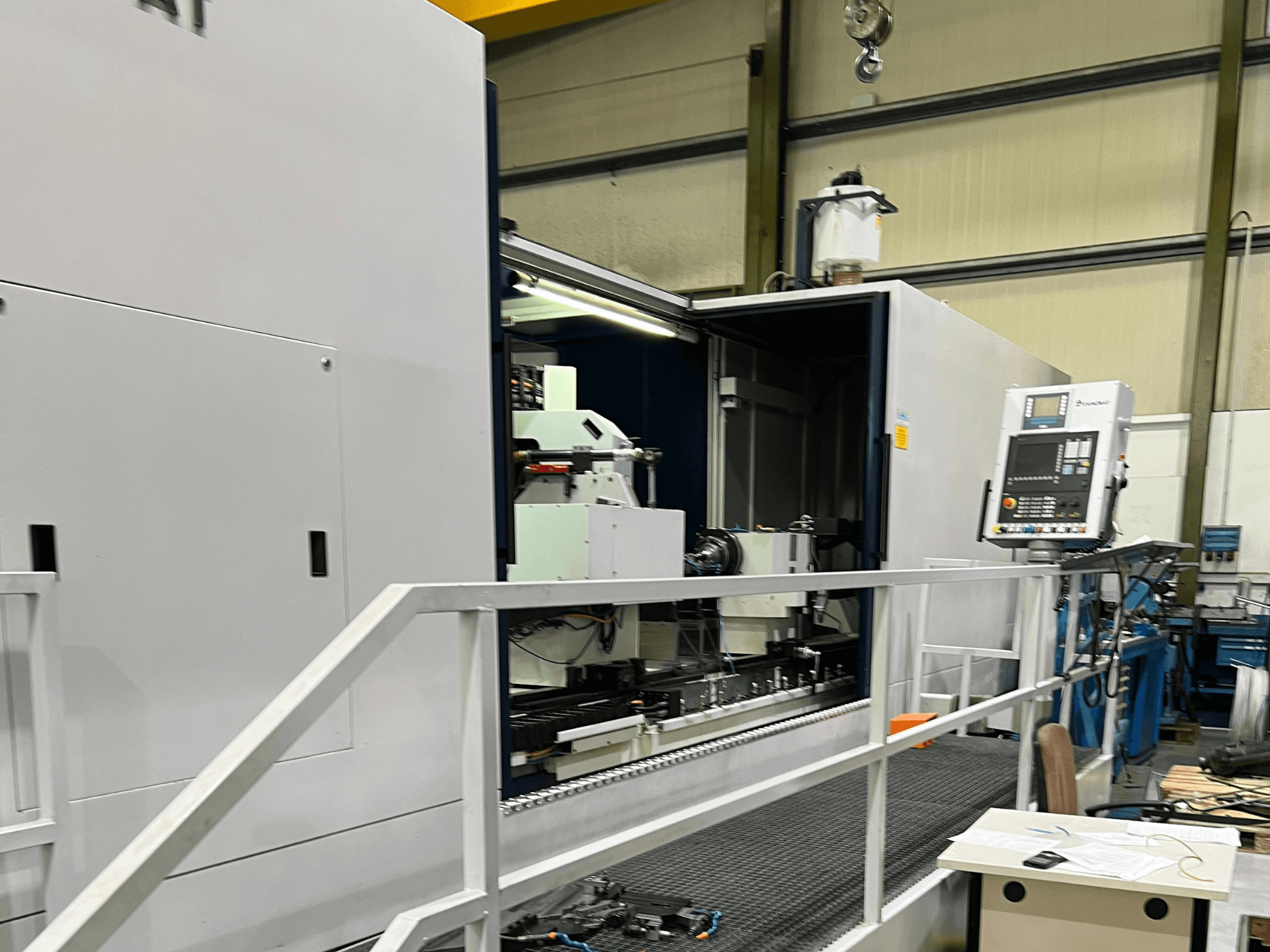 Centro de maquinagem CNC com vista lateral aberta, mostrando os controlos, o suporte de ferramentas e o componente principal no interior. Os pormenores da marca não são visíveis.