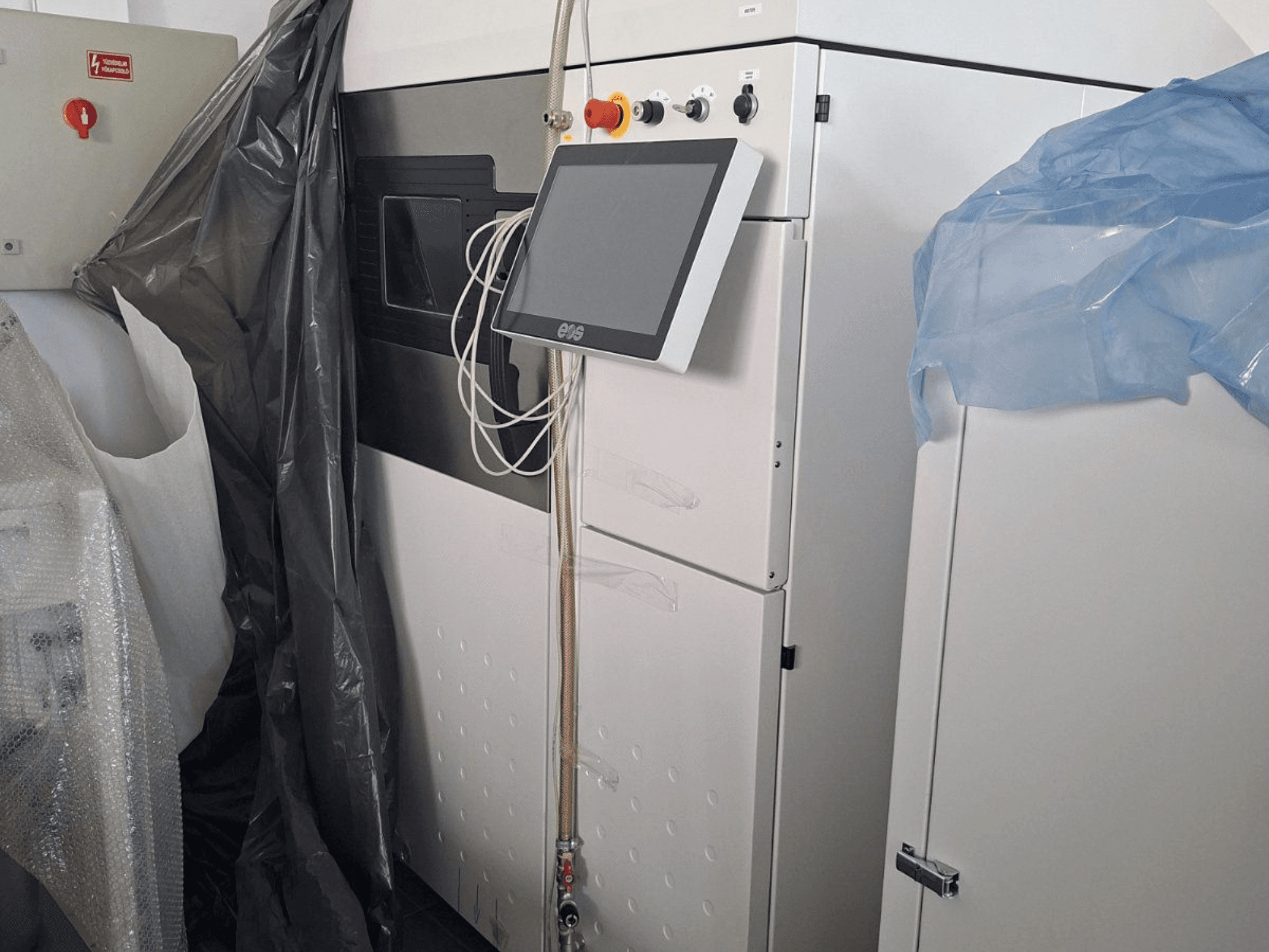 Vista frontal da impressora 3D em metal EOS M 290, com ecrã tátil, painel de controlo e coberturas de proteção.