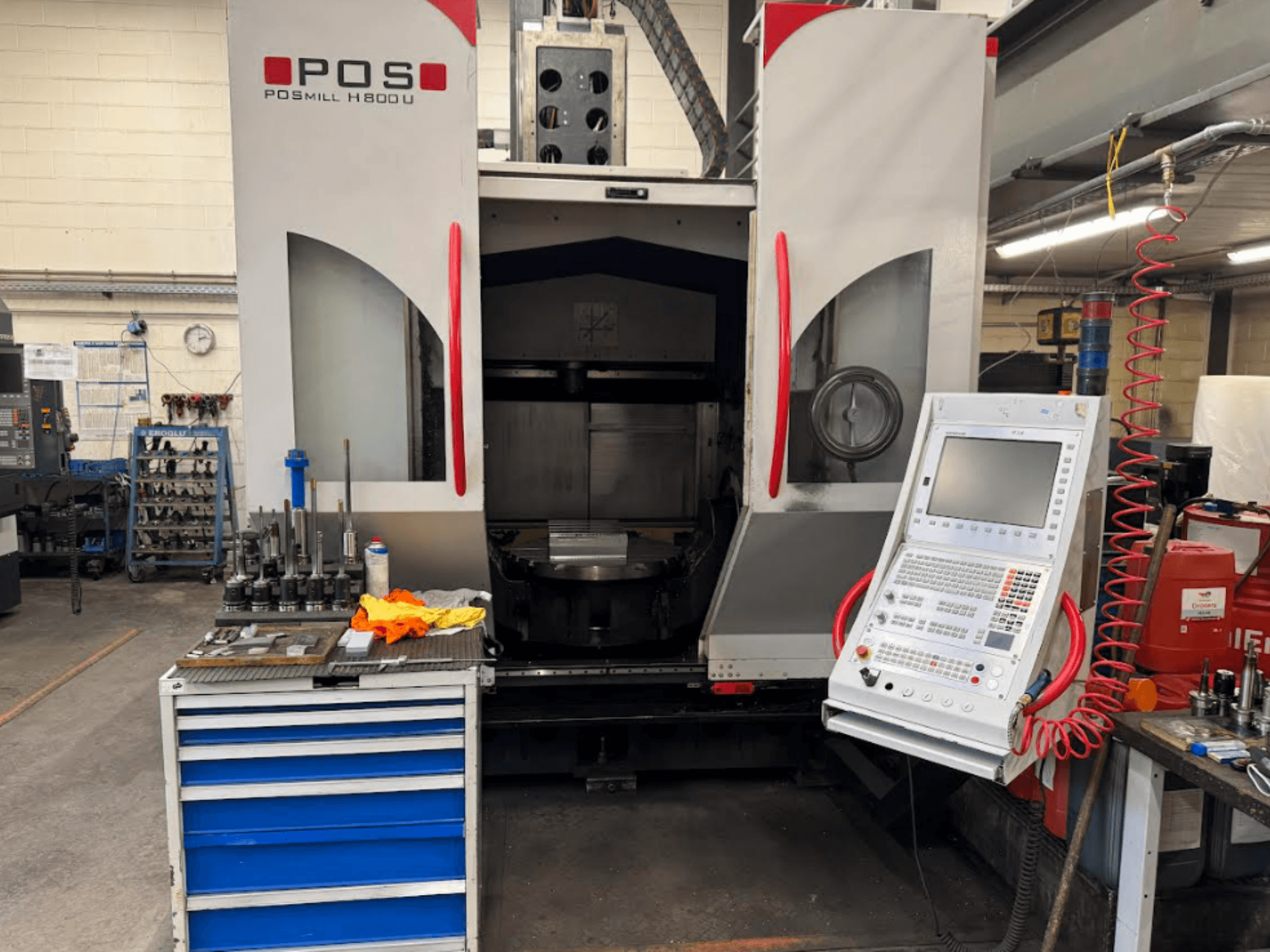 Máquina CNC POSMILL H800 U vista de frente, mostrando o painel de controlo e a área de trabalho com ferramentas e equipamento nas proximidades.