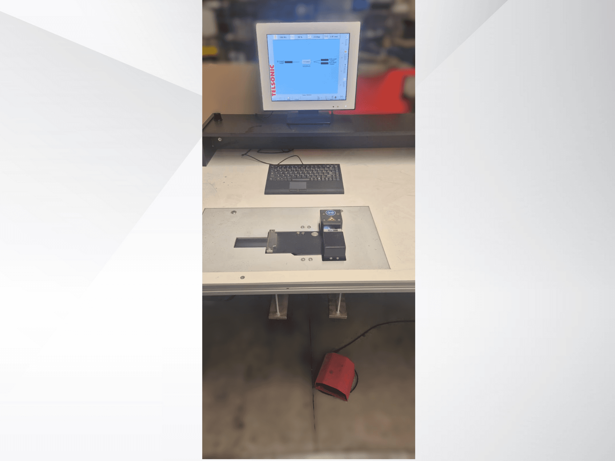 Vista de cima para baixo de uma estação de testes com um monitor de computador, um teclado e um painel de controlo com um botão e uma luz verde.