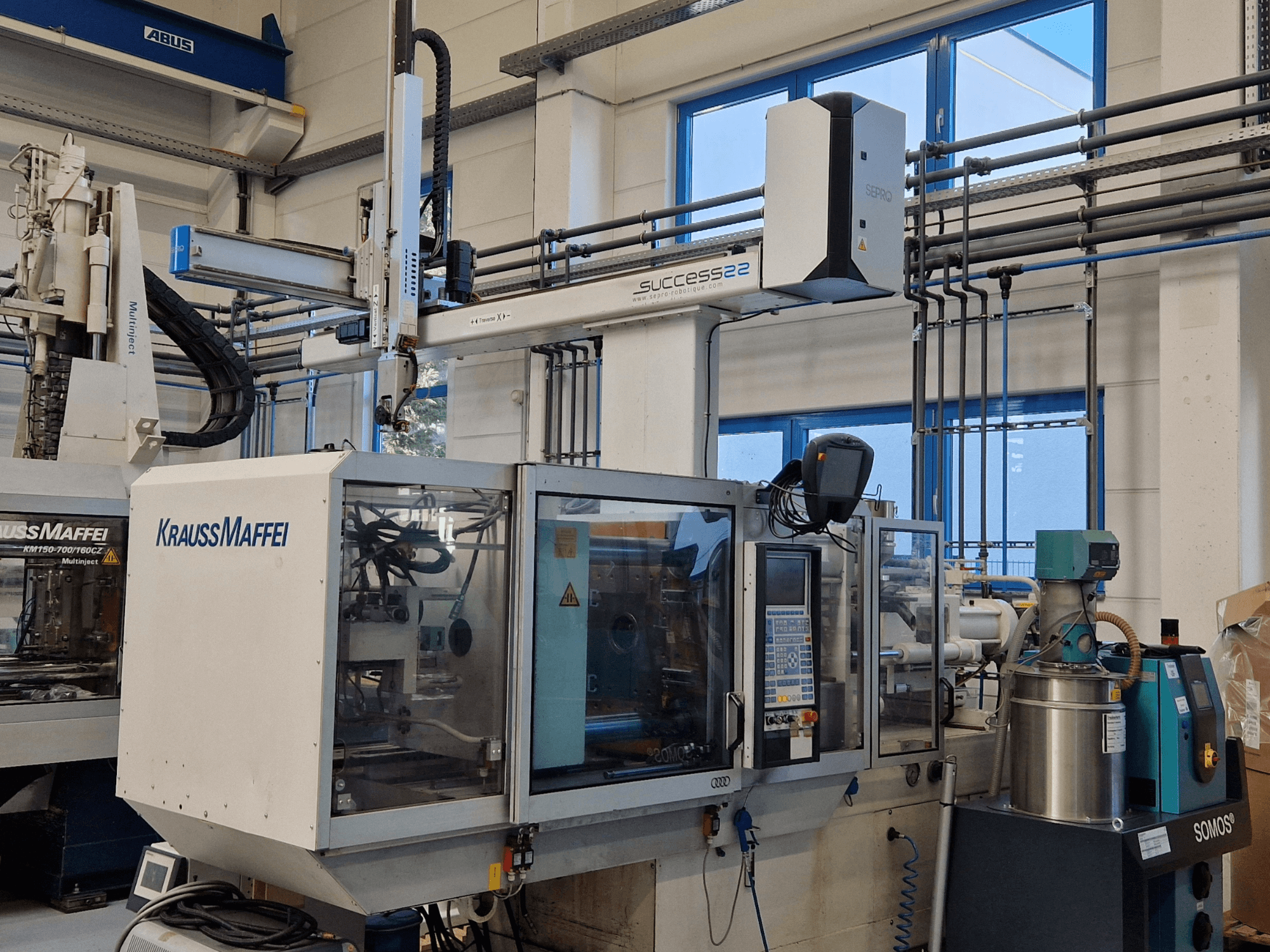 Máquina de moldagem por injeção KraussMaffei Success 22 com painel de controlo, vista de frente numa fábrica.