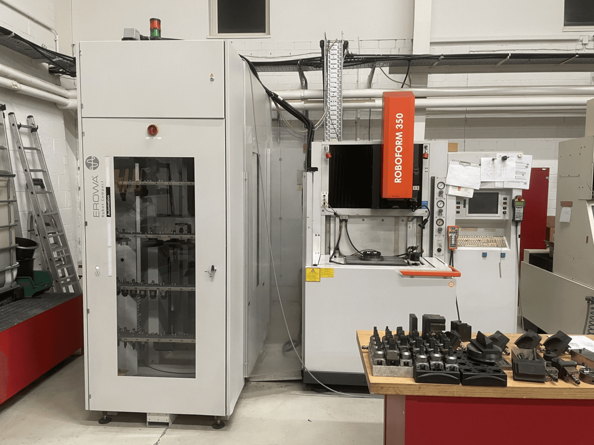 Máquina de electroerosão CHARMILLES Roboform 350, vista frontal, com ferramentas expostas numa mesa e equipamentos adjacentes.