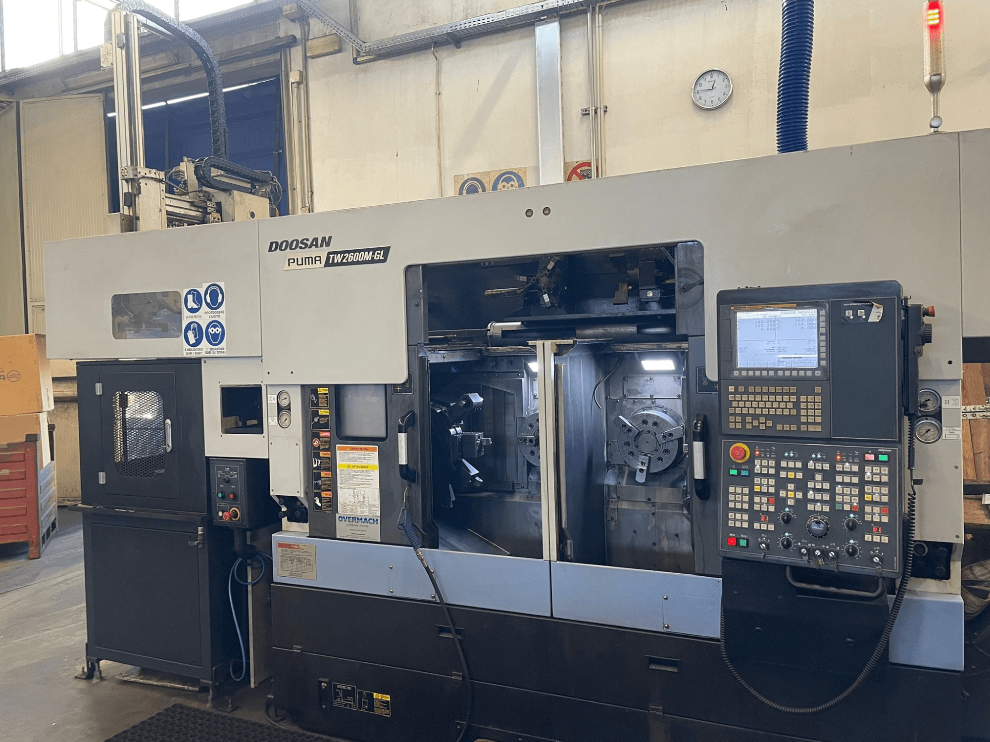 Torno CNC Doosan Puma TW2600M GL, vista frontal, mostrando o painel de controlo digital e o interior da máquina com suportes de ferramentas.