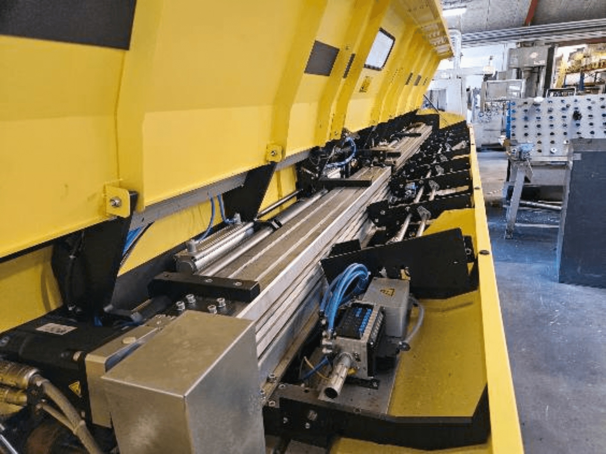 Vista de grande plano de uma máquina hidráulica amarela com componentes metálicos e esteiras transportadoras, com mangueiras e peças electrónicas.